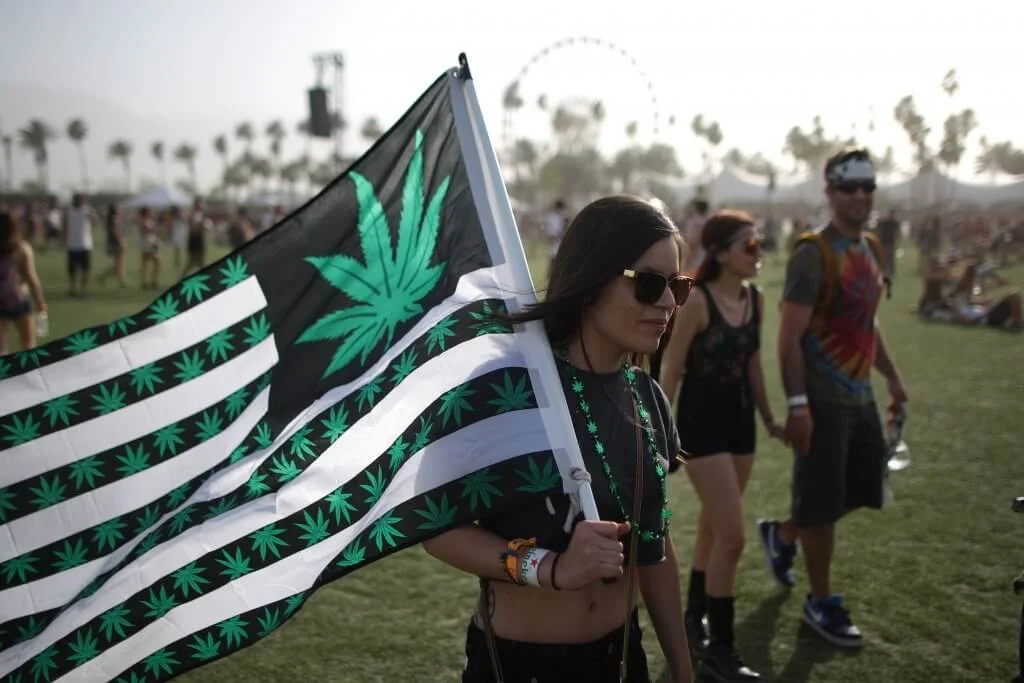 Una mujer porta una bandera de Estados Unidos con dibujos de hojas de cannabis durante el festival estadounidense de música de Coachella.