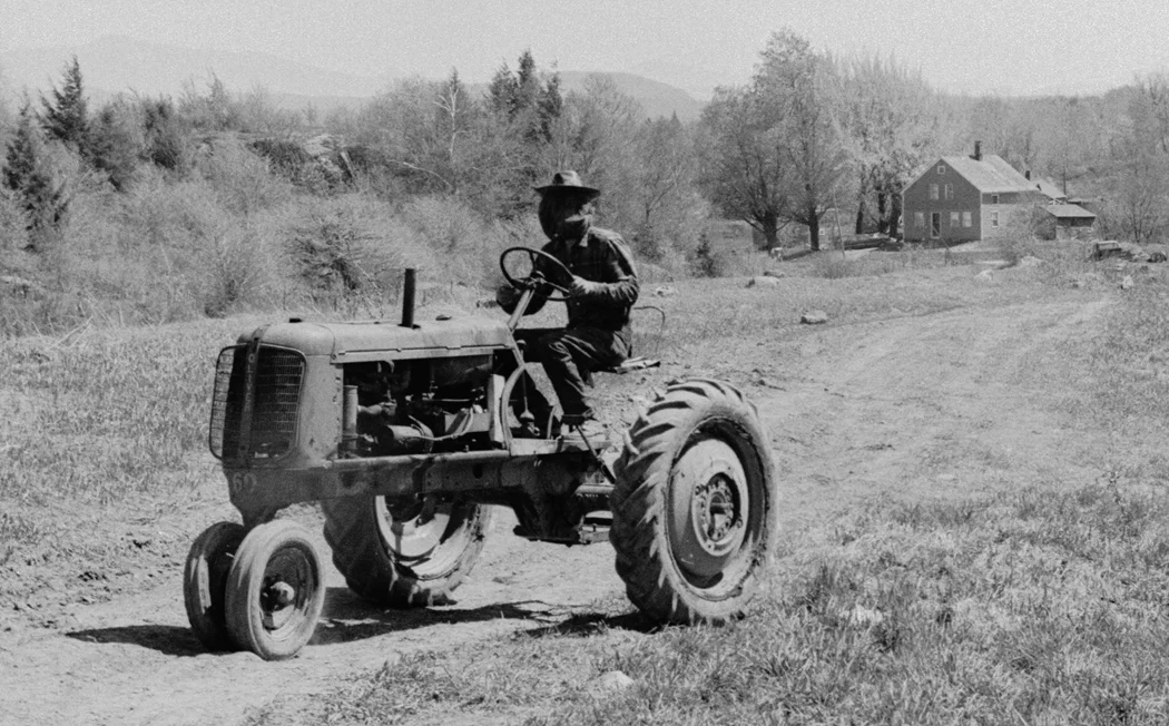 ca 1972, French Hill commune, St. Albans, communard in a mosquito headnet, driving a 1950's Oliver tractor borrowed from the Plouffe family in the house in the background.