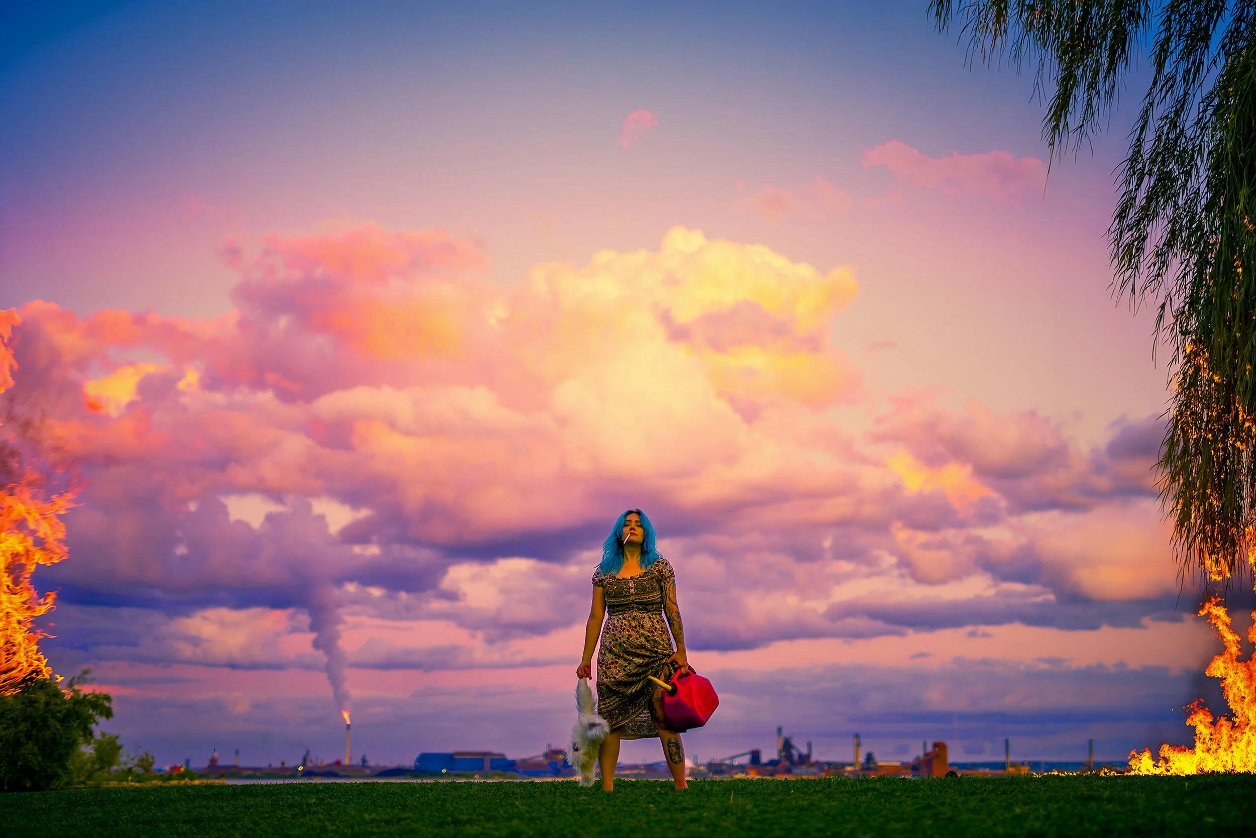 A woman with blue hair and tattoos standing outdoors at sunset, carrying a red bag and a stuffed animal, with colorful clouds in the sky and trees on either side.