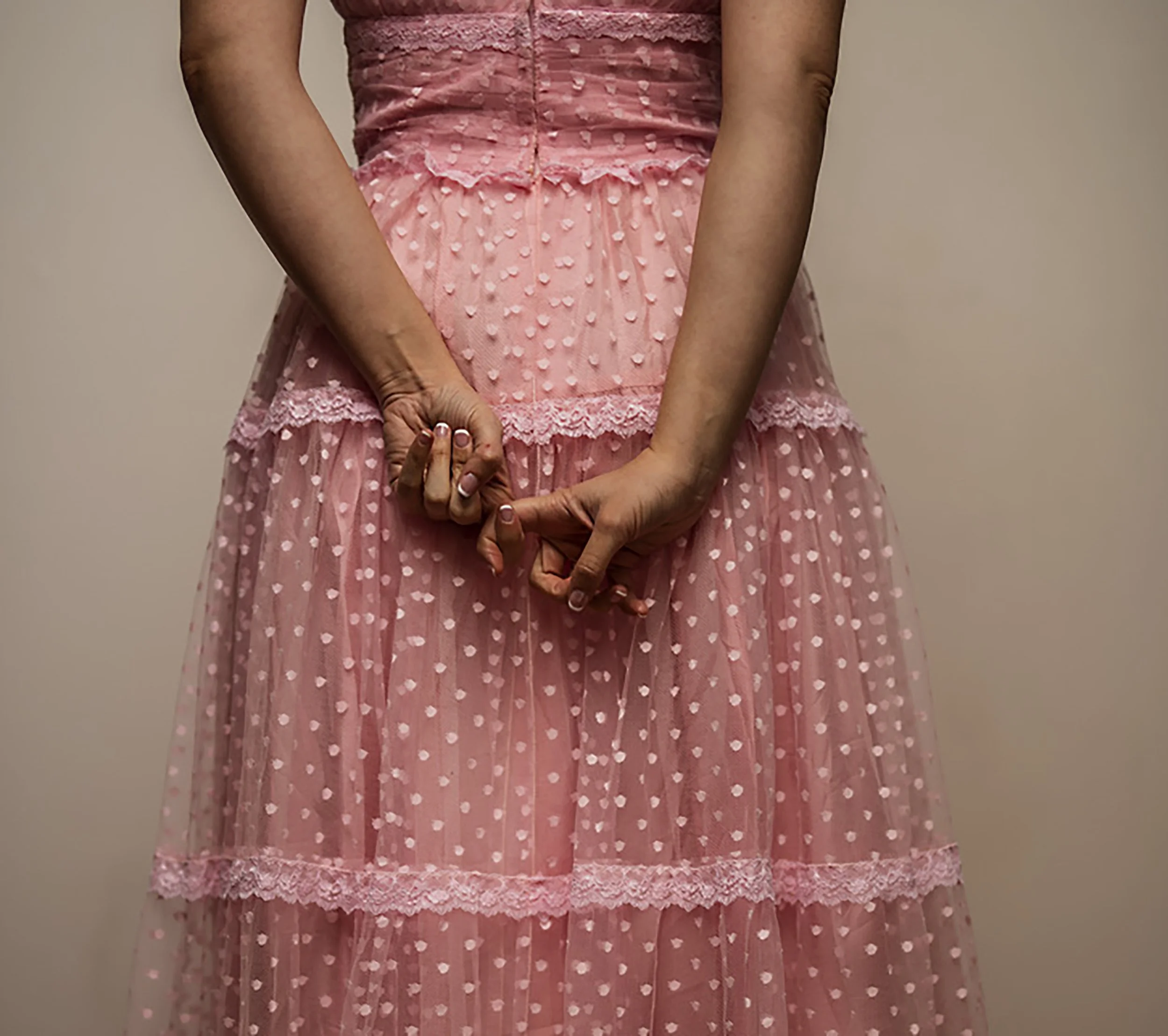 Close-up of a woman in a pink dress with a polka dot pattern and lace details, standing against a plain background.