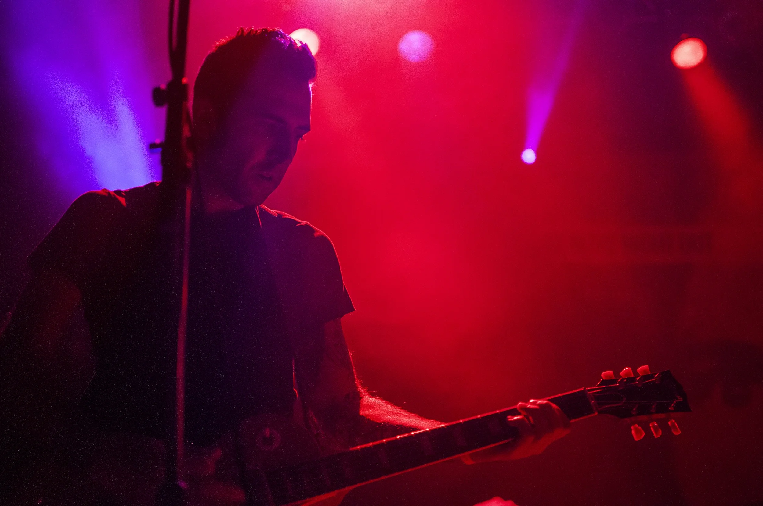 A person playing a keyboard on stage with pink and purple stage lights illuminating the scene.