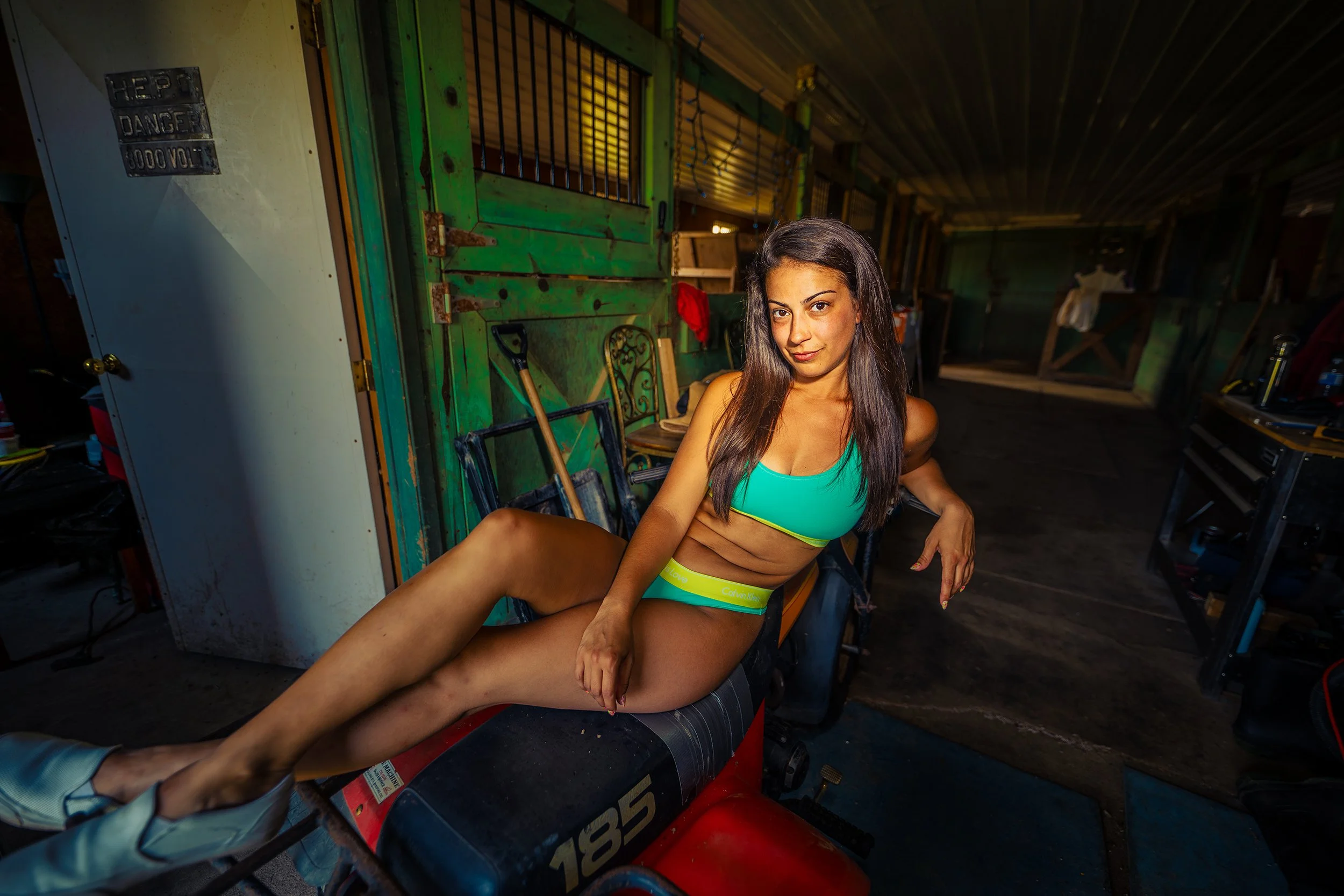 A woman in athletic wear sitting on an exercise machine in a cluttered garage or workshop.