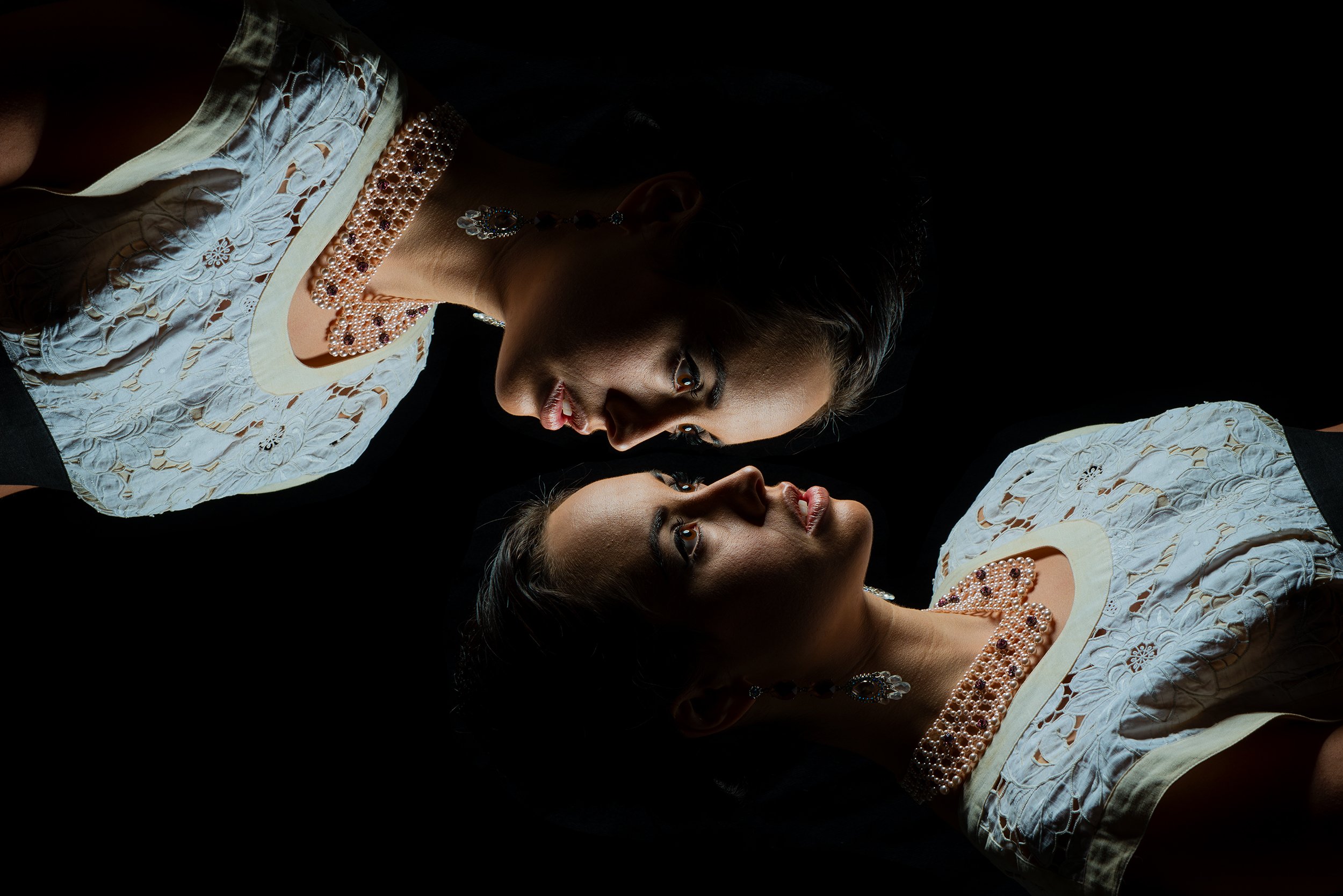 Two women dressed in traditional embroidered clothing and jewelry, facing each other in a close-up shot in a dark setting.
