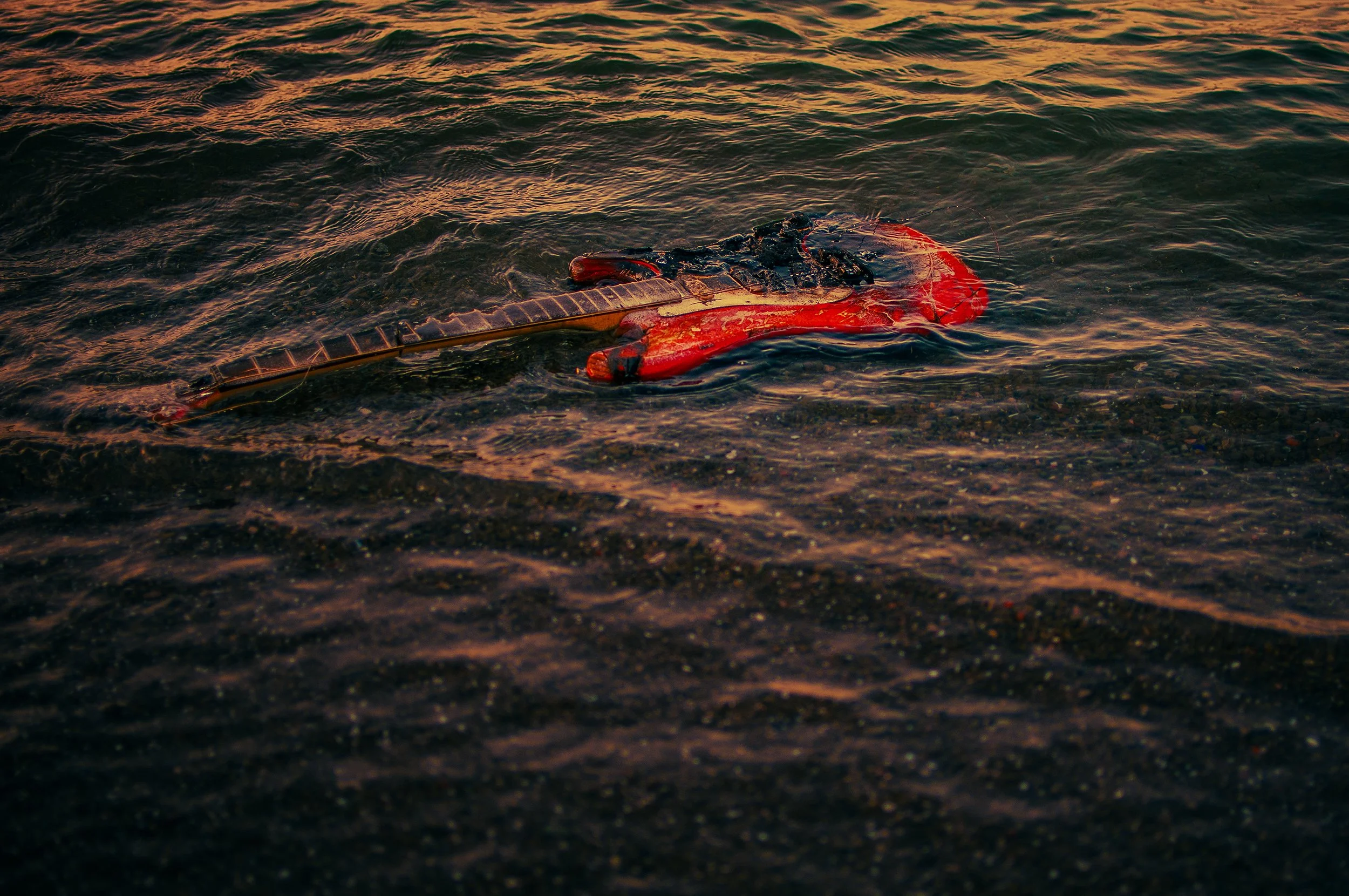 A red lobster trapped under a plastic bottle in a body of water, with the water's surface reflecting the sunset colors.