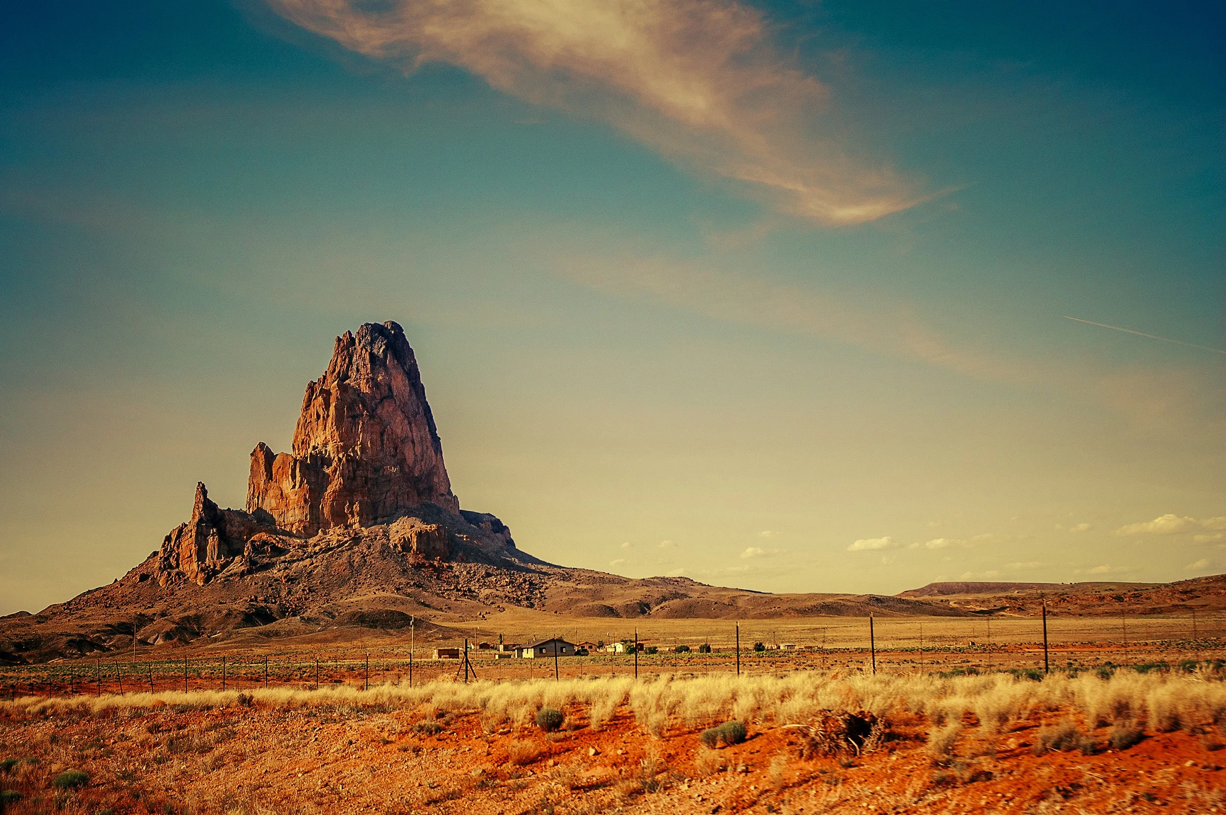 A desert landscape with a prominent rocky mountain under a mostly clear sky with some clouds.