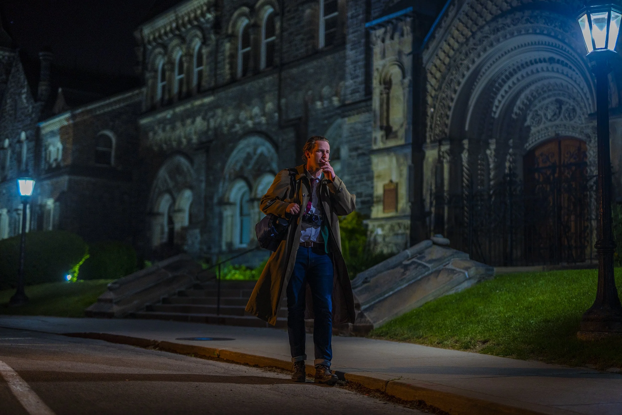 A man walking at night in front of a historic building with intricate architecture, illuminated by streetlights.
