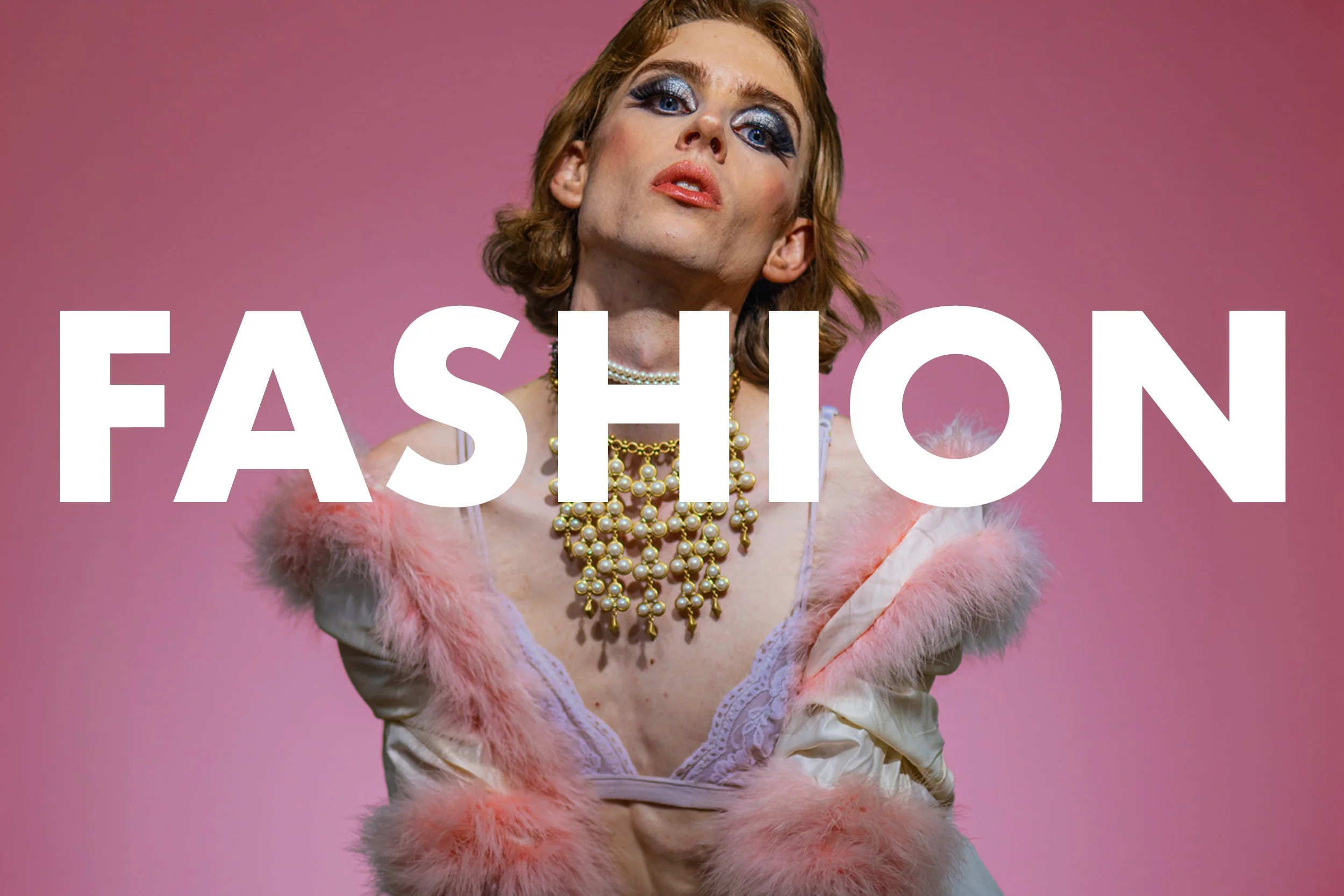 A person with red hair and heavy makeup wearing multiple pearl necklaces, a pink faux fur coat, and satin lingerie against a pink background with the word "FASHION" in large white letters.