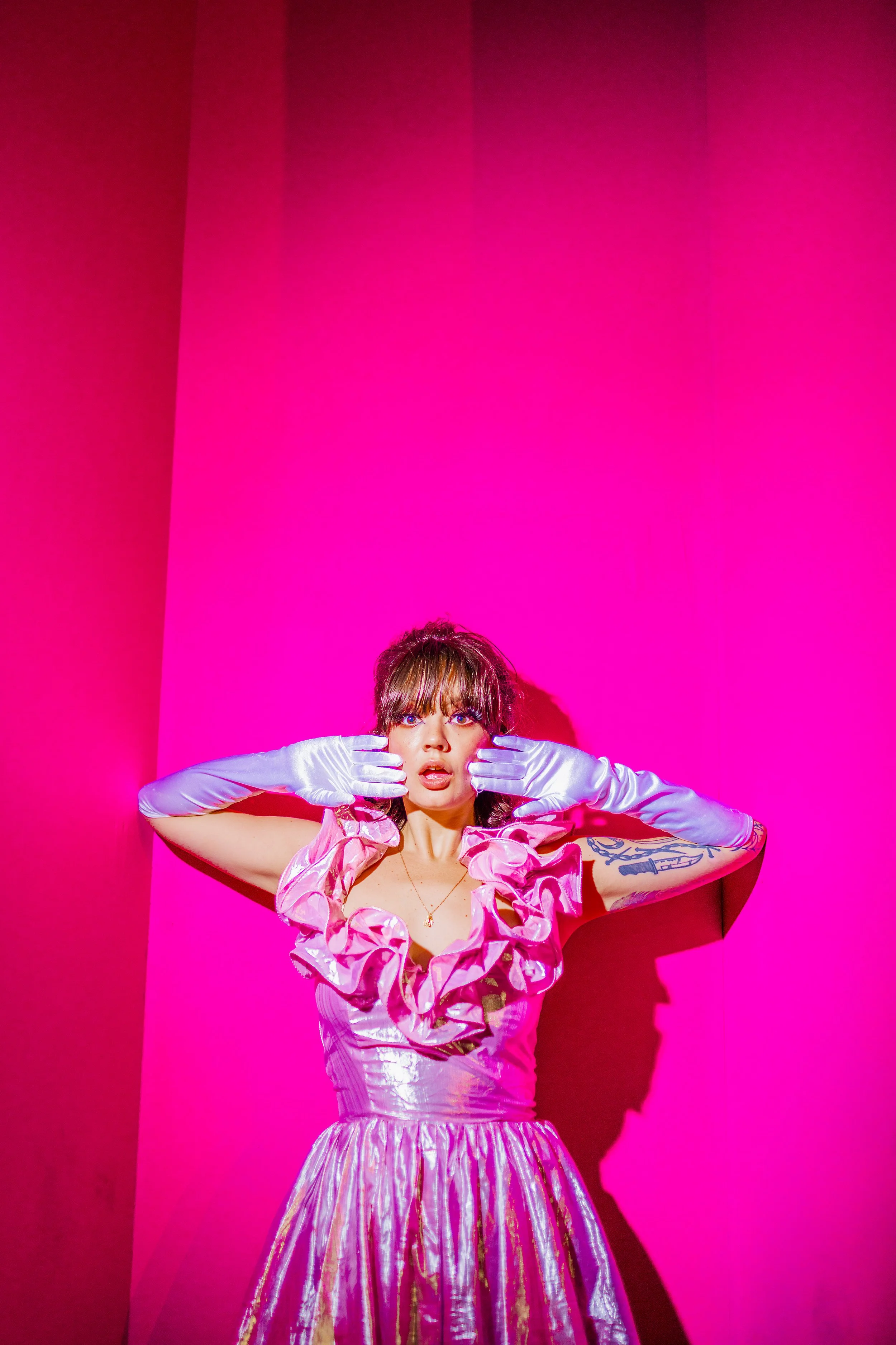 Woman in pink shiny dress and white gloves posing against pink background