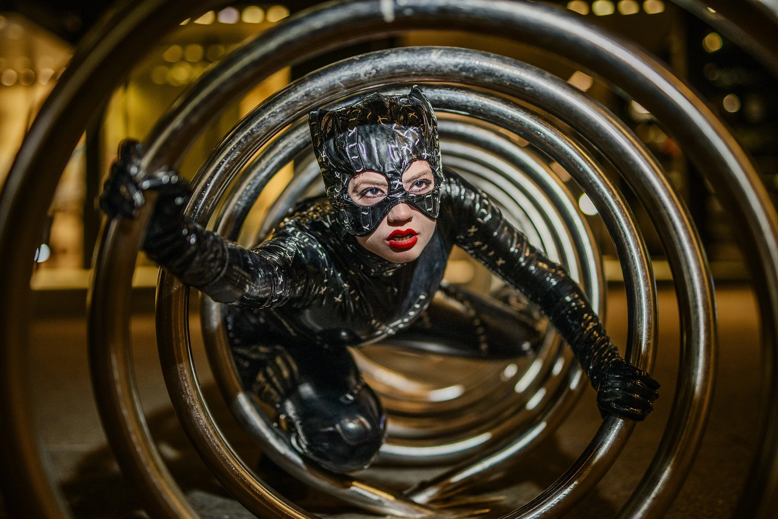 A person in a shiny black latex outfit and mask crawling through a tunnel of metallic hoops.