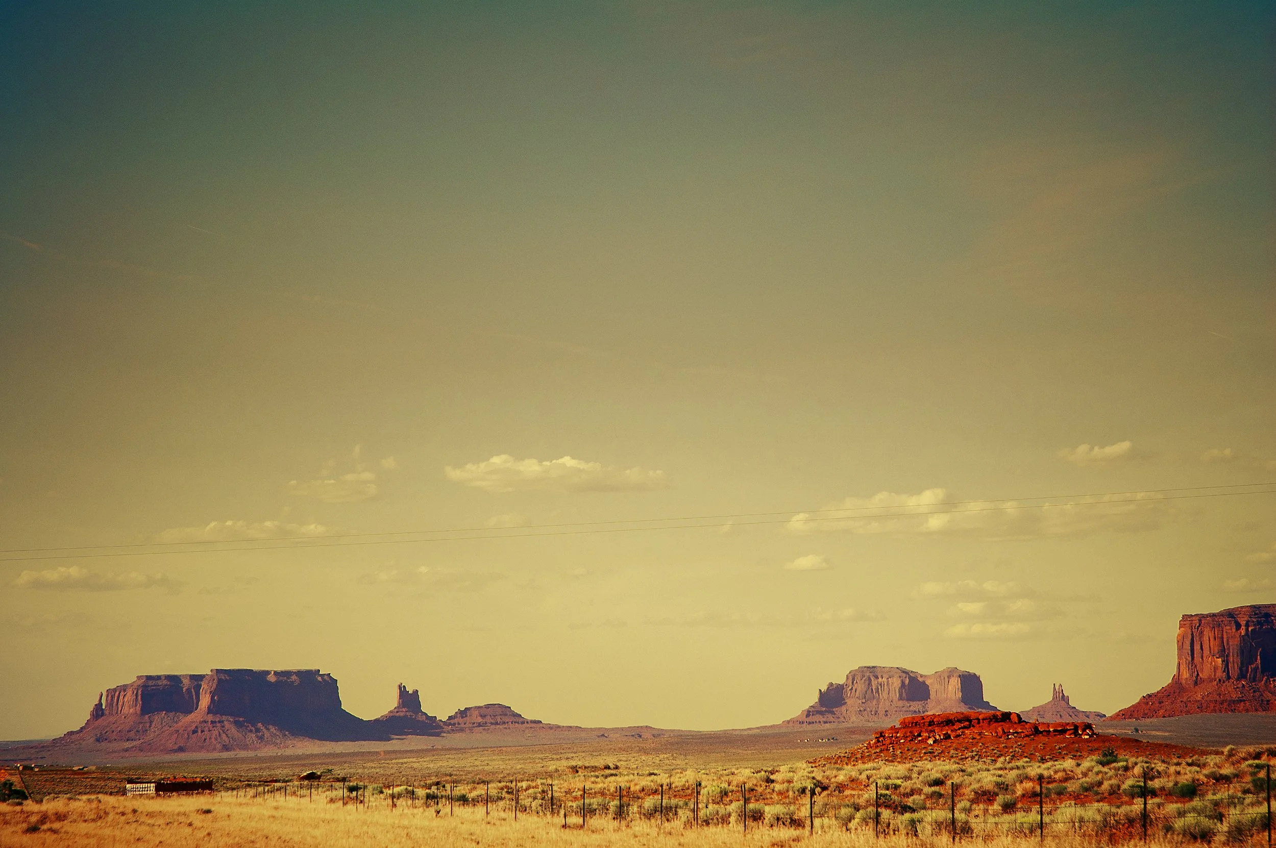 A desert landscape with large rock formations and mesas under a sky with distant clouds.