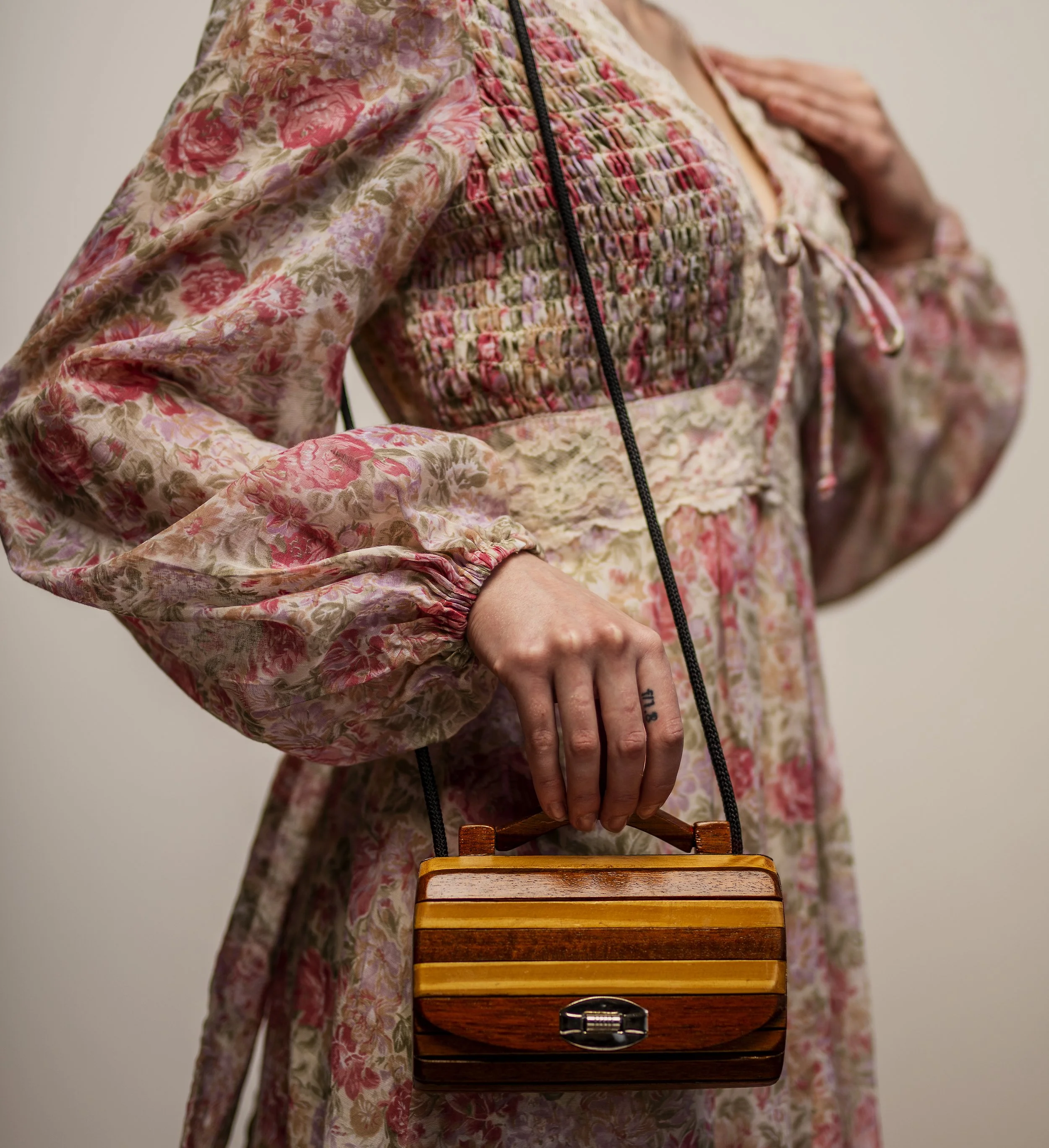 Person wearing a floral dress holding a wooden handbag.
