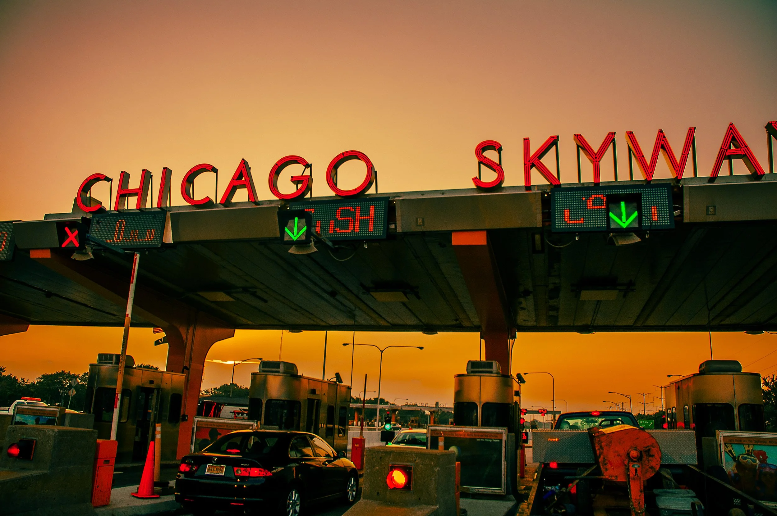 Chicago Skyway toll booth at sunset with neon signs and traffic.