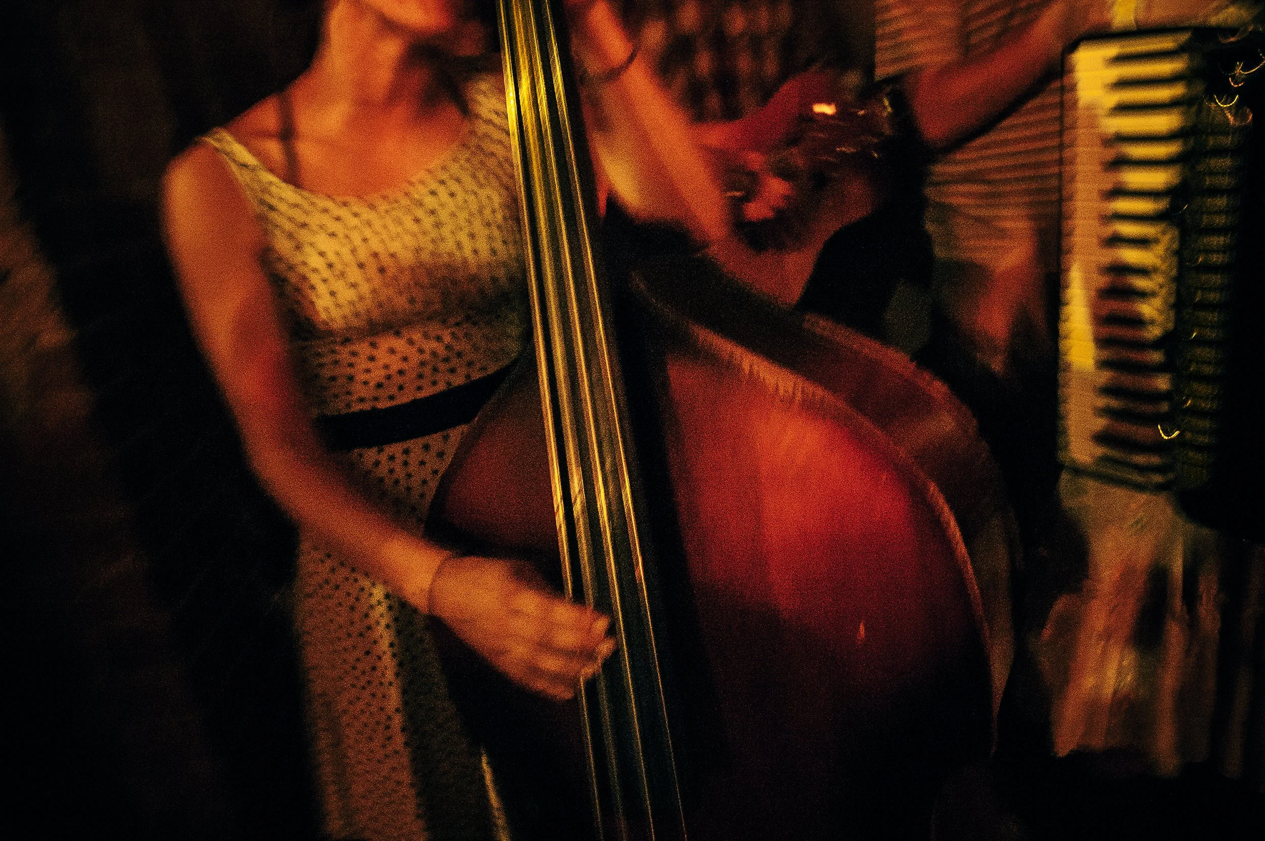 Two women playing a red electric guitar and a keyboard in a dimly lit setting.