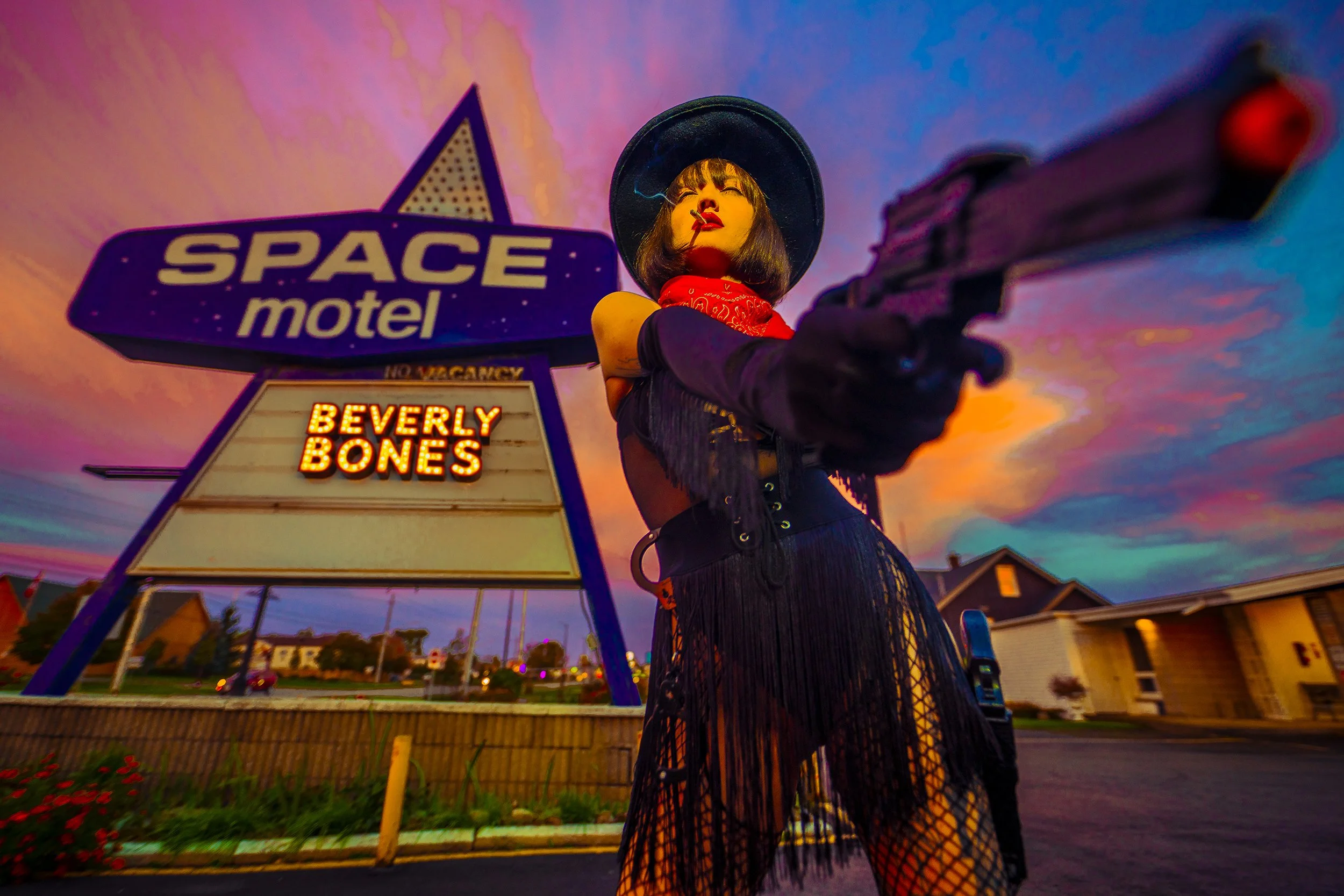 A woman in a black hat, red bandana, and black fringe outfit holding a gun, standing in front of a neon-lit motel sign that reads 'SPACE motel' and 'BEVERLY BONES' with a colorful sunset sky in the background.