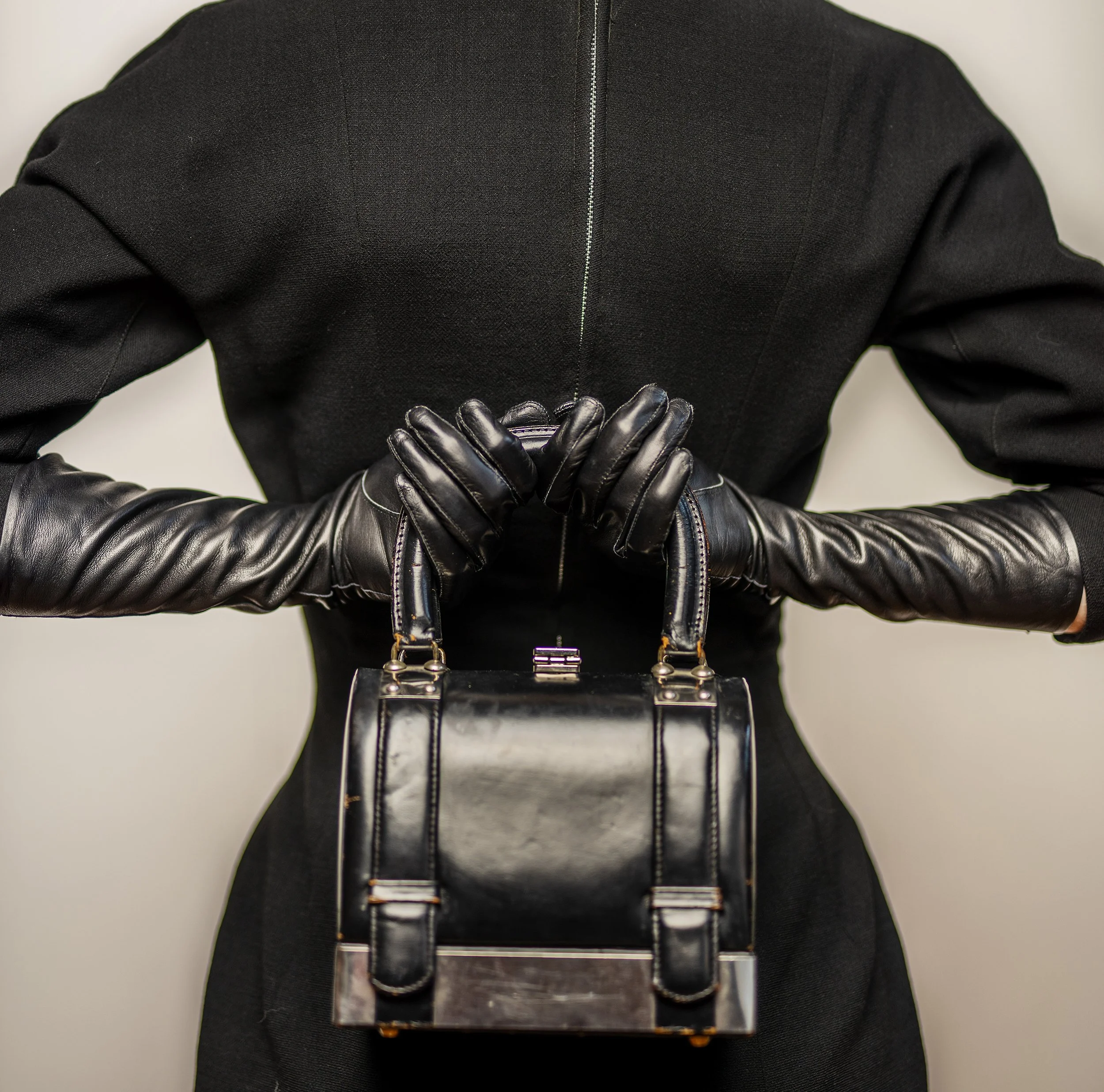 People wearing black jackets and black gloves holding an object, with a plain background.