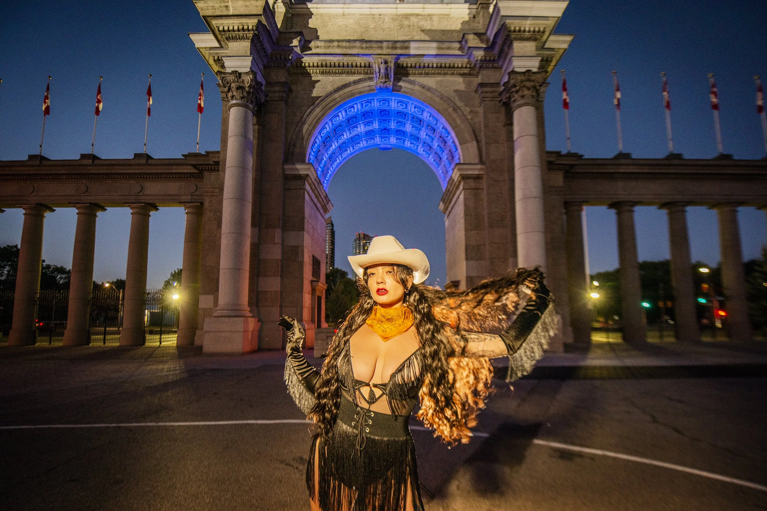 Woman dressed in a cowboy-themed costume standing in front of a lit archway at night.