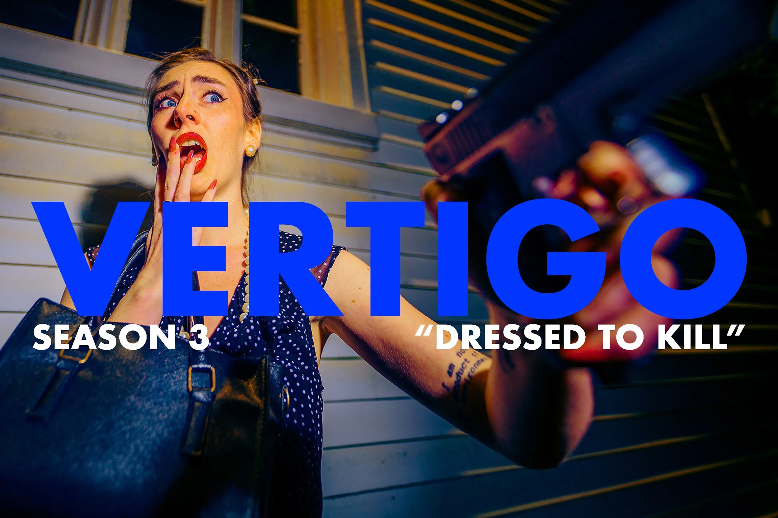 A woman with blue eyes, red lipstick, and pearl earrings, holding a gun pointed at the camera with a surprised or frightened expression. She is wearing a navy polka-dot dress, standing in front of horizontal metal panels. The text overlay reads 'VERG