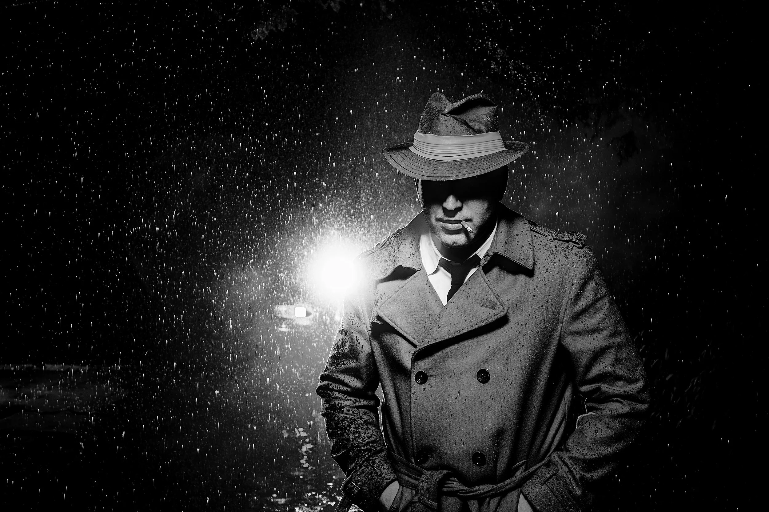 A man wearing a trench coat and a wide-brimmed hat with a ribbon, smoking a cigarette in the rain at night, with raindrops visible amidst backlighting.