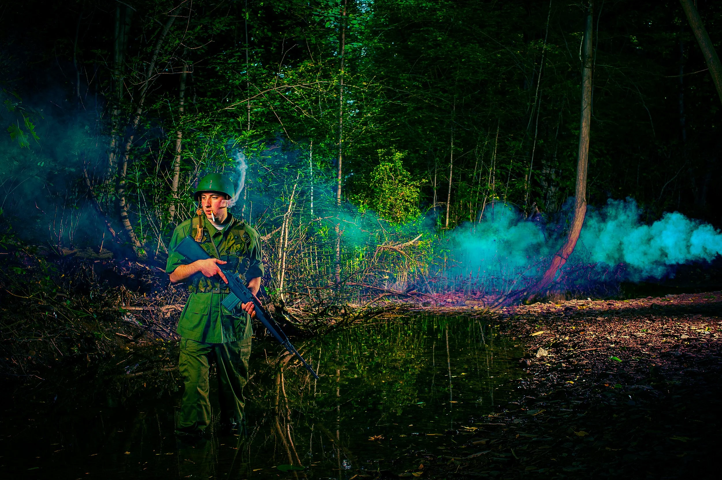 A soldier in green uniform and helmet standing in a forest at night, holding a rifle, with smoke and illuminated trees around.