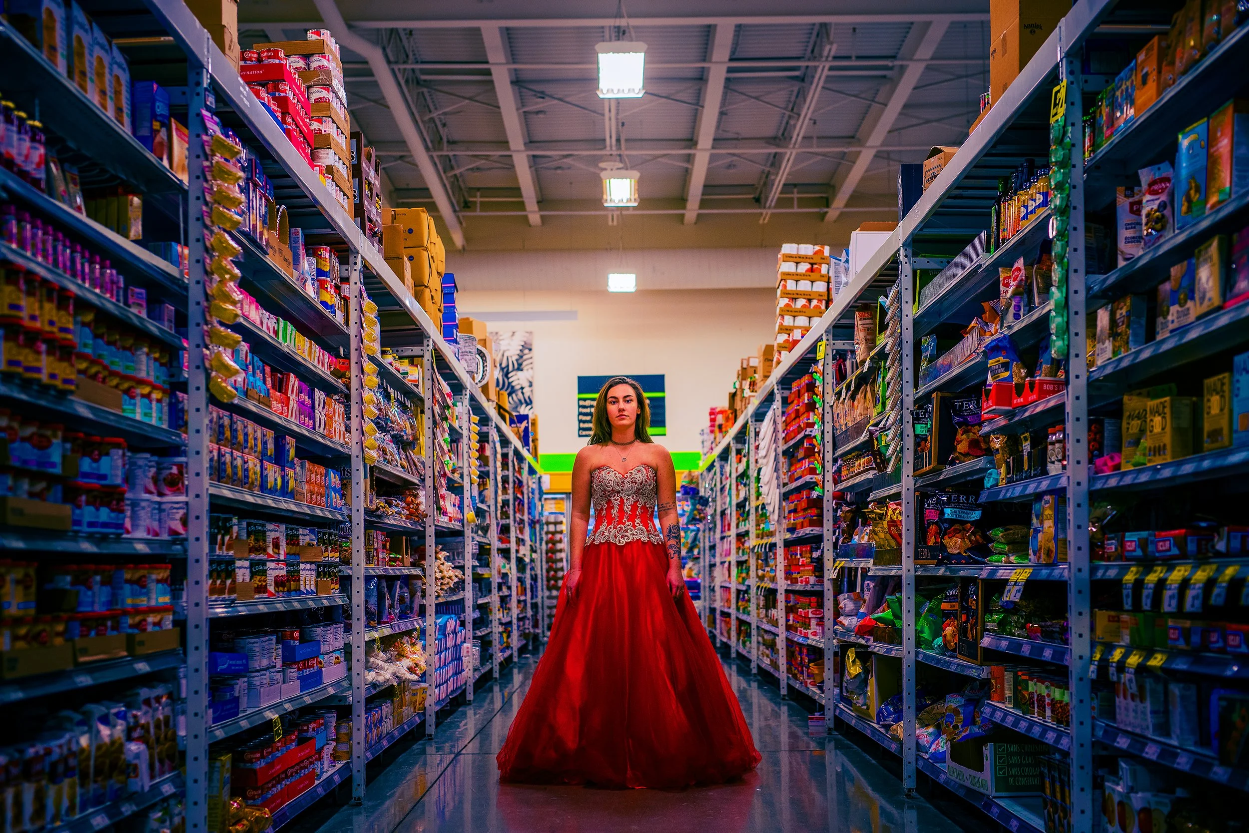 A woman in a red dress with lace details standing in the aisle of a grocery store, surrounded by shelves of food and snacks.