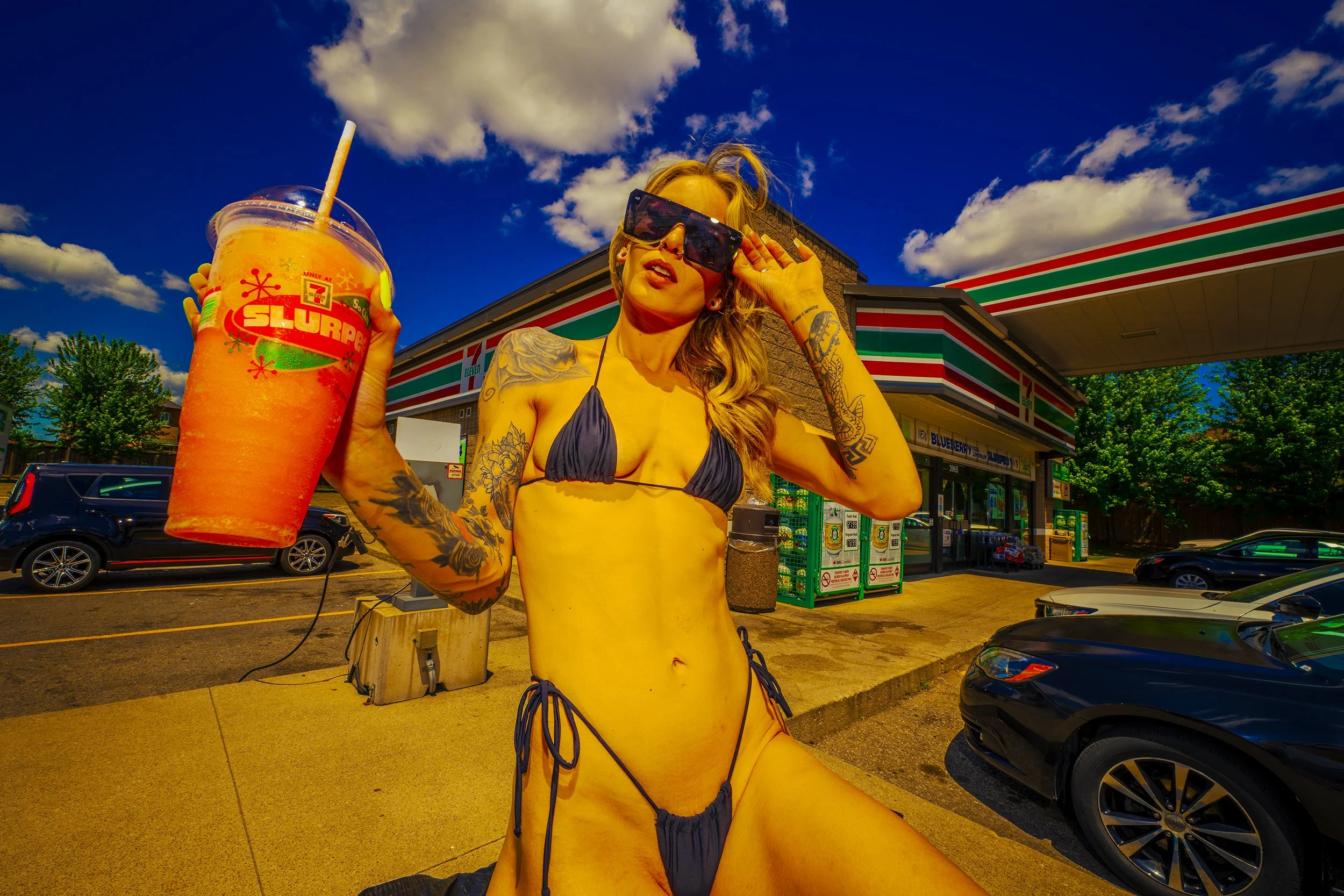 Woman in a bikini with sunglasses outside a convenience store, holding a large slush drink.