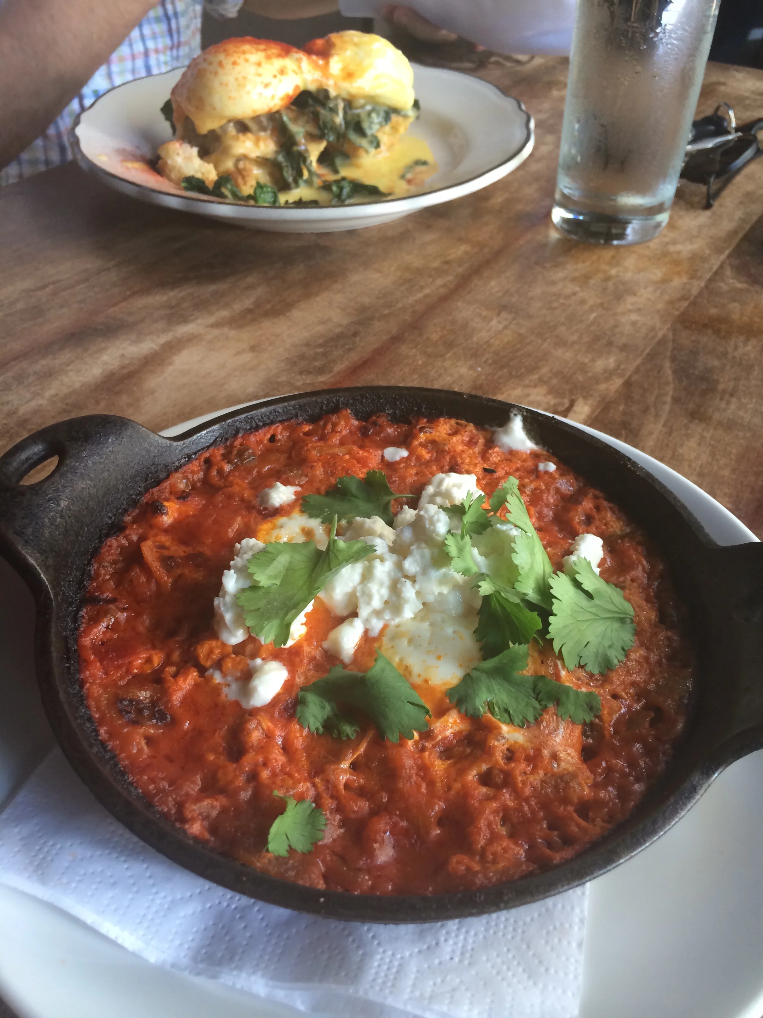Atrás os Eggs Pork Belly Benedict que meu marido pediu. Em primeiro plano, Shakshuka: ovos assados em molho picante de pimentões e tomate.