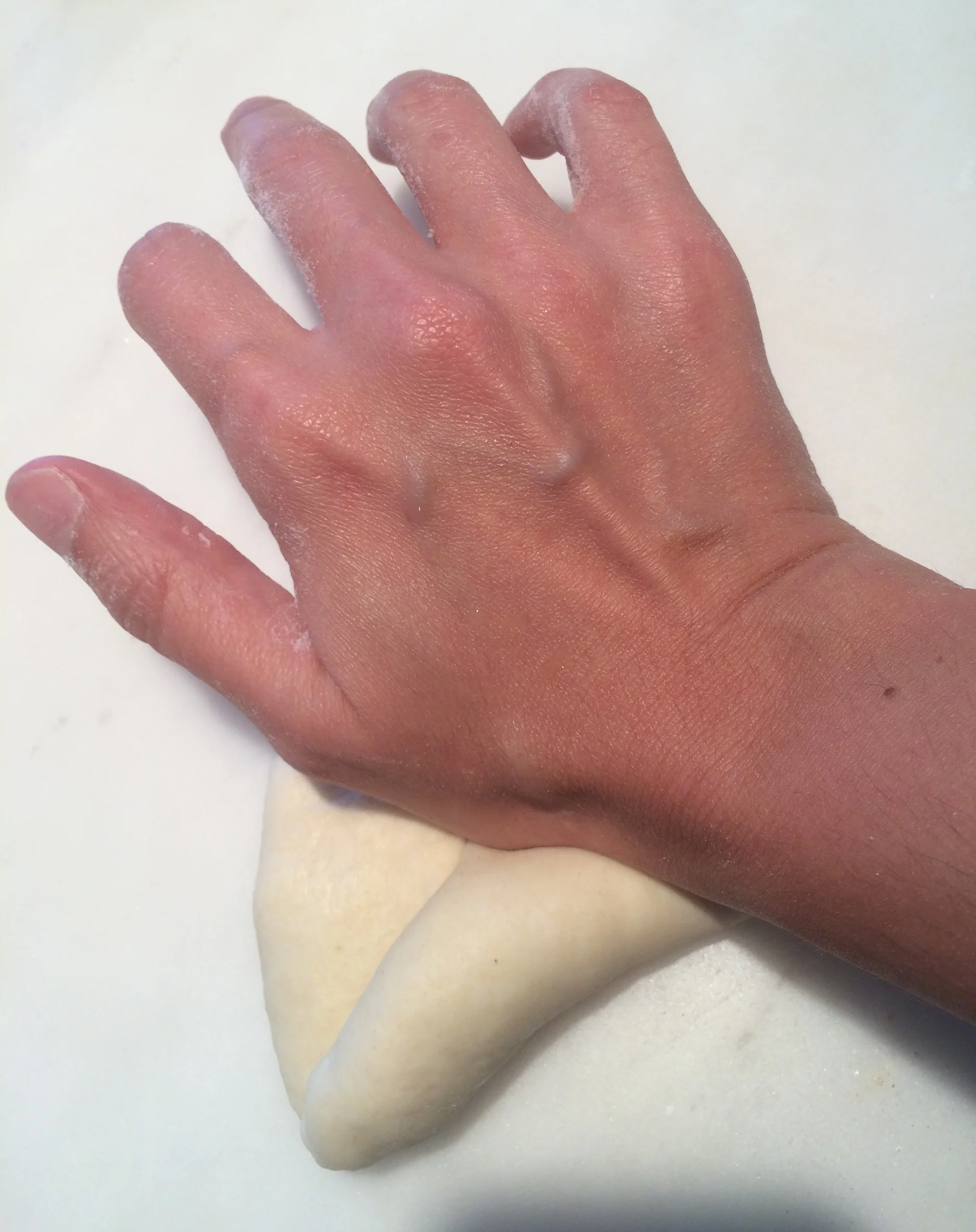 Enrole a massa sobre si mesma aos poucos, apertando cada volta com a base da mão, para que o miolo fique bem fechadinho. Ao terminar de enrolar, belisque as bordas para emendar o pão direitinho, pra ele não correr o risco de abrir enquanto estiver crescendo ou assando.