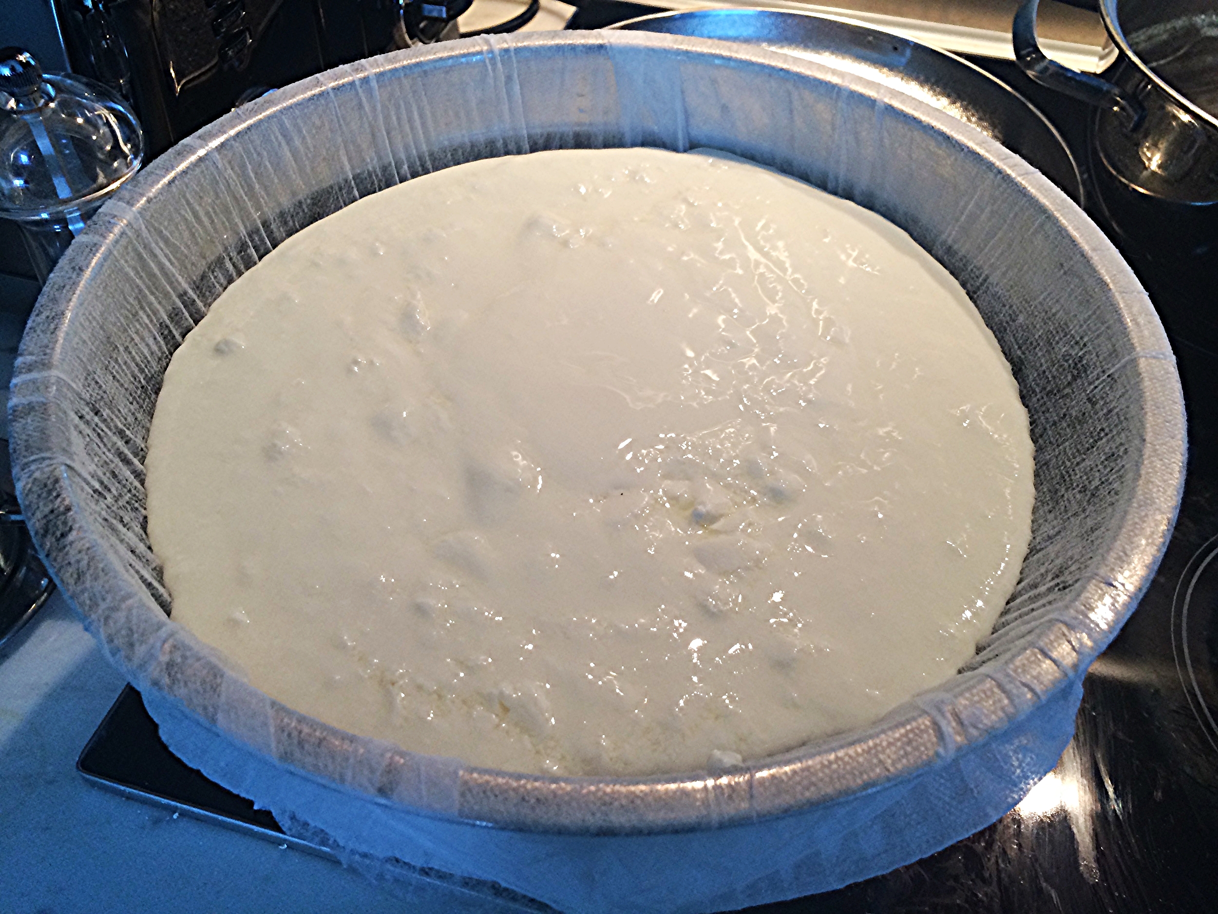 Coloque uma liguinha de borracha forte (ou várias) sob a borda externa da vasilha, pra segurar a touca suspensa do fundo. Se você não tiver, pode colocar a touca sobre uma peneira. Tampe o iogurte e leve à geladeira pra escorrer por 8 horas, no mínimo!