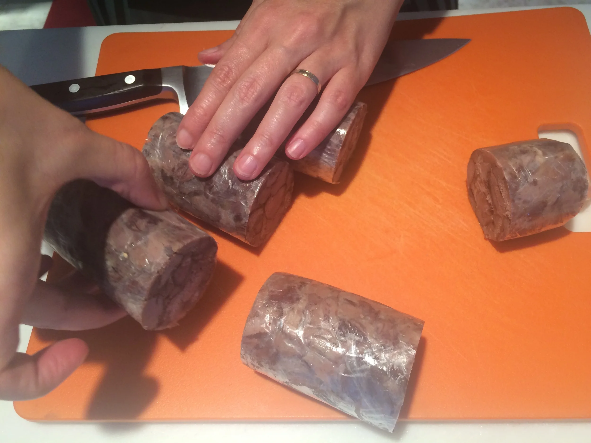 Retire a ballotine de cordeiro da geladeira somente quando o forno já estiver quente, o molho e o purê já prontos. Corte-os no tamanho desejado (aqui eu usei 4 dedos meus como referência para a altura). Retire imediatamente o plástico filme. 