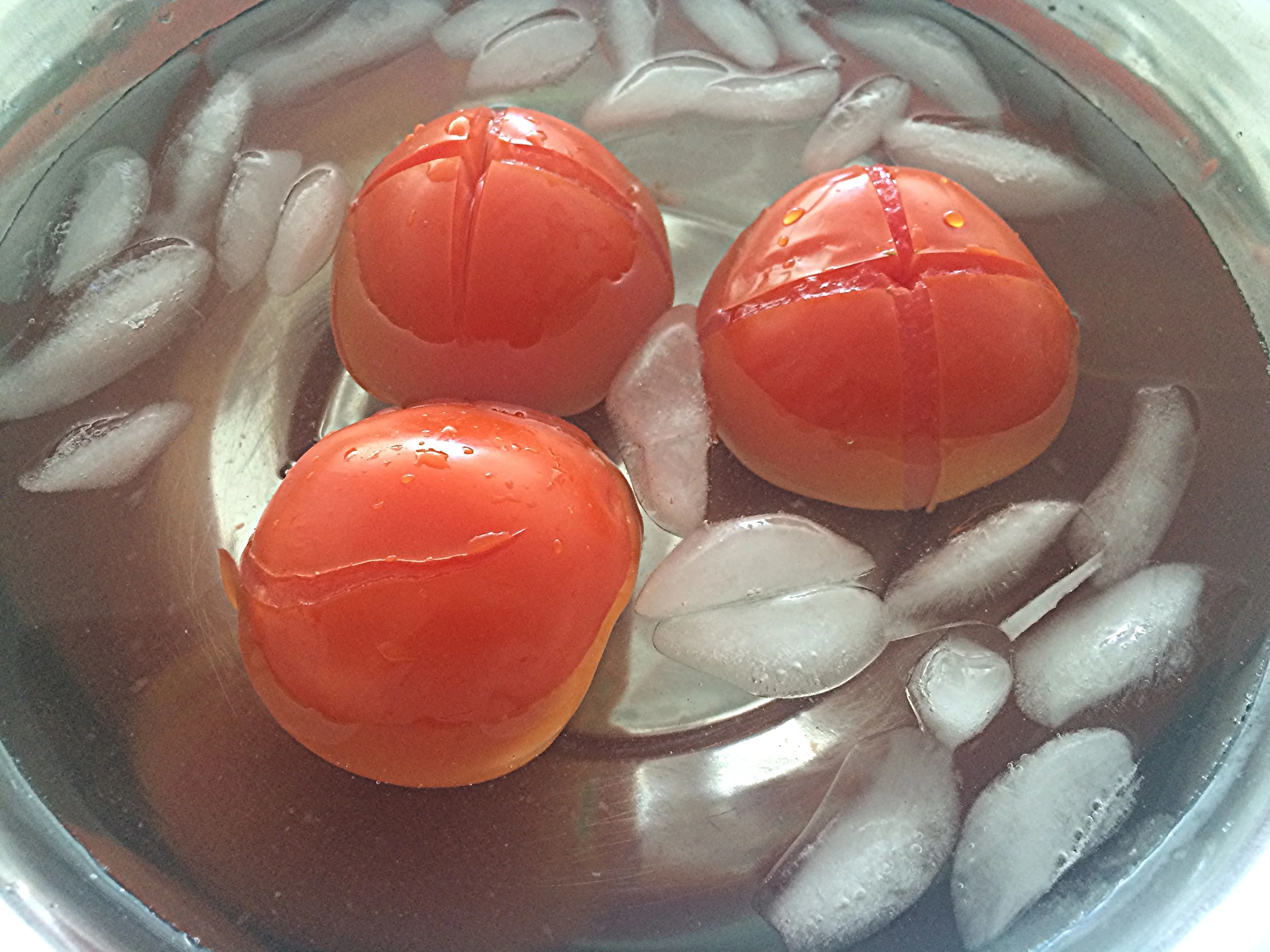 Numa tigela já preparada com um banho maria invertido (água com gelo) mergulhe os tomates recém-retirados da água quente para interromper o processo de cocção. Aguarde até que eles estejam frios. 