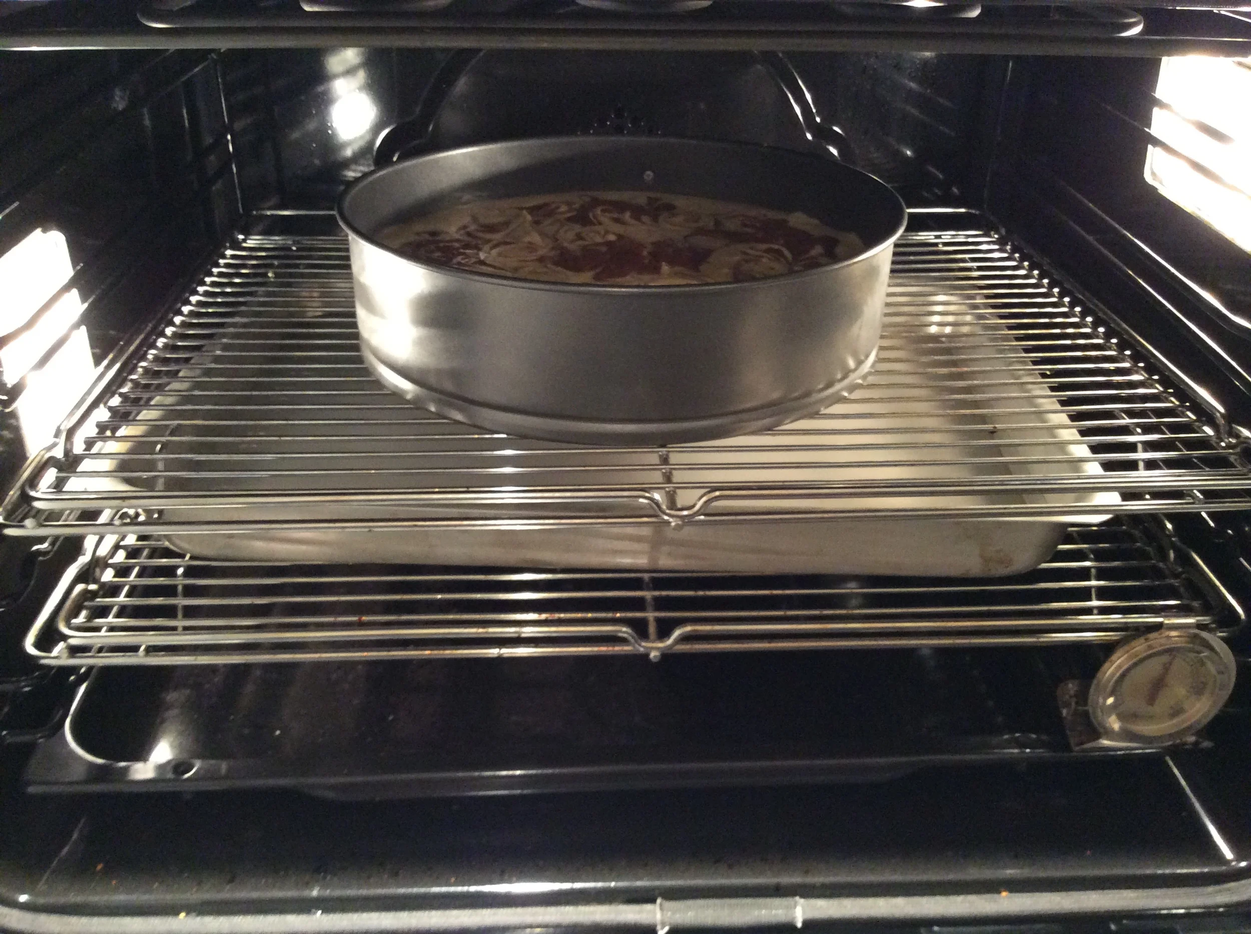 Leve a cheesecake ao forno, já com a forma cheia de água quente na grade de baixo, por aproximadamente 1 hora e quinze. Ela estará pronta quando as bordas estiverem firmes, mas o centro ainda estiver faltando um pouco pra cozinhar. Para ver o ponto, bata a mão levemente na porta do forno fechado e veja como a superfície se comporta. Se o centro tremer levemente, está ok. Desligue o forno, coloque uma colher de pau entreabrindo a porta dele e deixe a cheesecake dentro por mais 1 hora. Faça o teste do palito, que deverá sair limpo. Coloque sobre uma grade para esfriar. Leve a geladeira até o dia seguinte. 