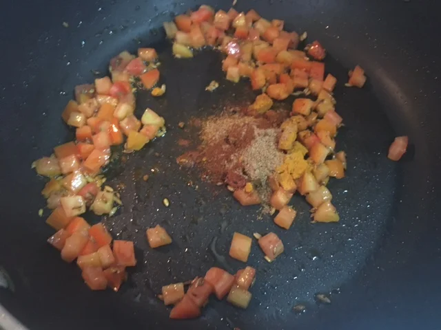 Adicione os tomates para cortar a cocção do cominho e evitar que ele queime. Junte as outras especiarias e misture para que elas liberem seu perfume pela casa. Cozinhe até que os tomates comecem a se desmanchar. Adicione o sal e o açúcar e misture bem.