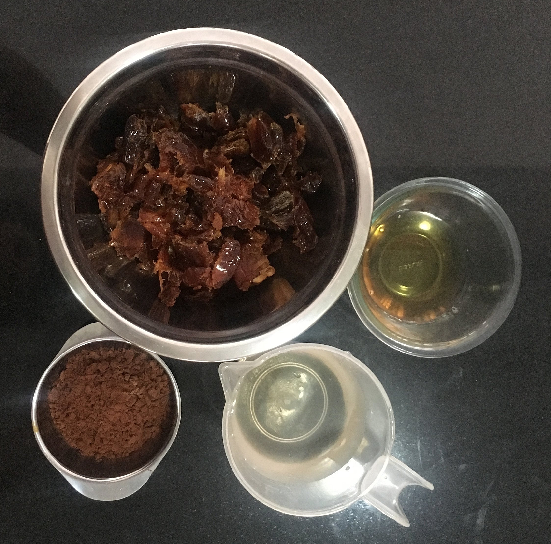 Descaroce as tâmaras, pese-as e coloque-as numa tigeja resistente ao calor. Faça a mise en place completa da pasta de tâmaras. Ferva a água e verta-a sobre as tâmaras - a quantidade será suficiente para cobri-las. Passe o café bem forte e adicione as duas colheres dele à tigela. Junte o cacau em pó peneirado, a bebida alcoólica (aqui na foto eu coloquei 2 colheres de uísque e uma de rum, mas pode ser tudo de uma coisa só) e misture. Deixe esfriar pra continuar a receita.