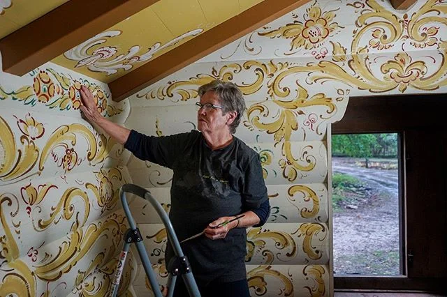 @salliedereus studies the original #Rosemåling design by the late Norwegian painter Sigmund Aarseth along the walls of @Binkhaven in #DoorCounty, Wisconsin. Once an apprentice of Sigmund herself, Sally continues the work onto the ceiling to match his unique 70's style using a dry brush technique in a modern telemark style. #ScandinavianAmerican