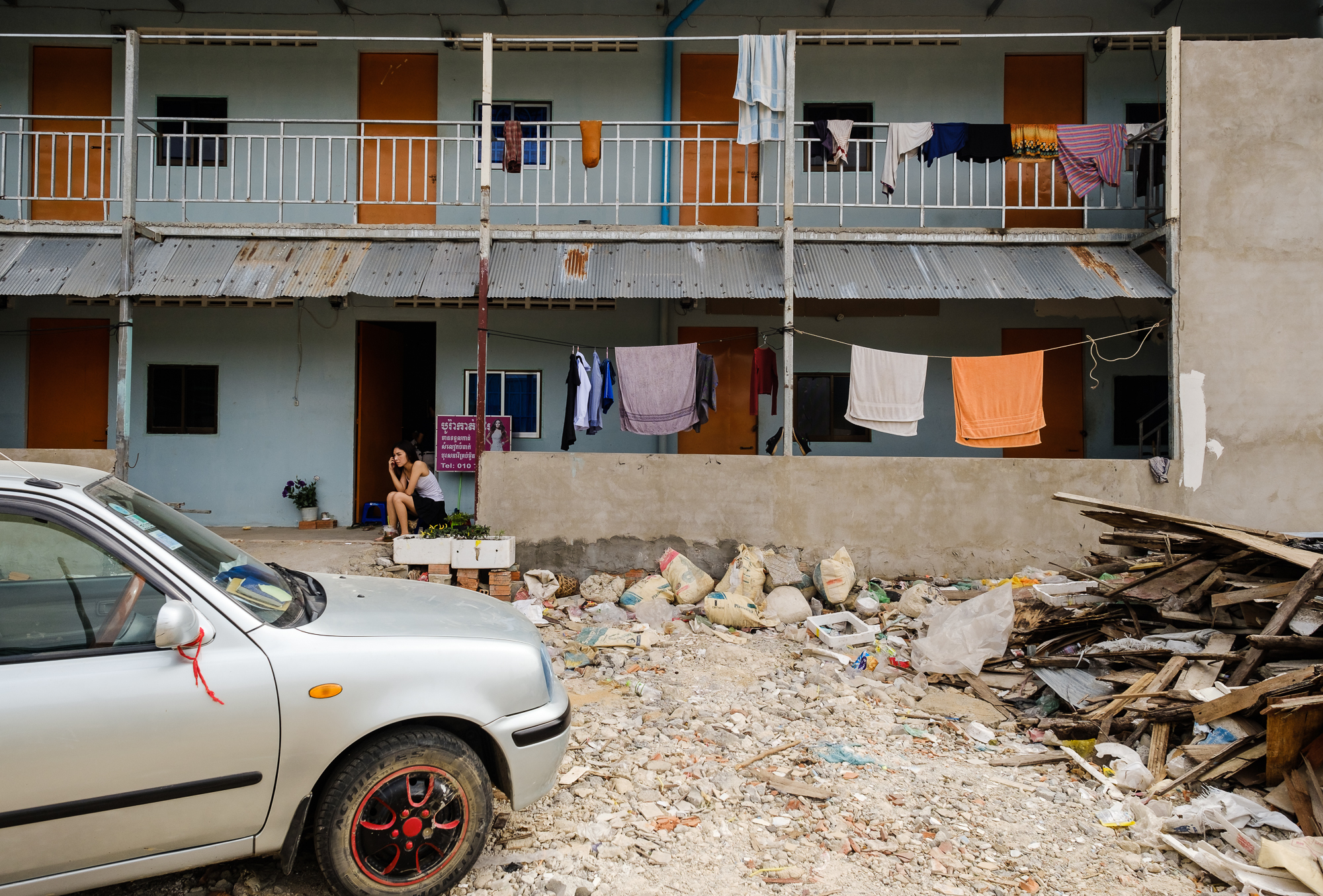 A woman sits outside her apartment amongst the rubble of 12.44, a government designated resettlement area that houses only a small amount of the once thriving Boueng Kak population.