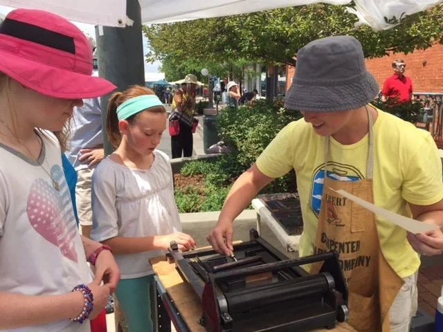 Elanor demonstrating inking on the proof press at the Cherry Creek Arts Festival