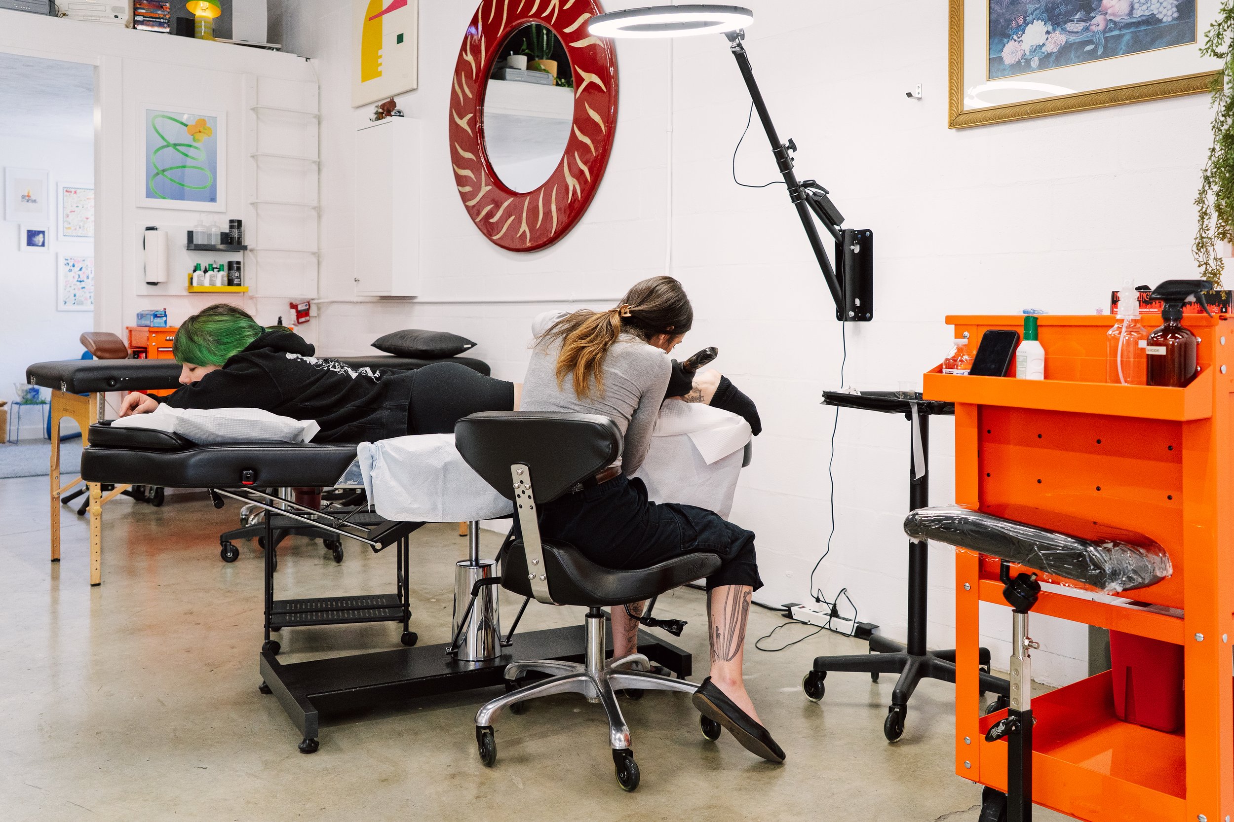 Tattoo artist at work in a bright, modern studio space with an orange tool chest.