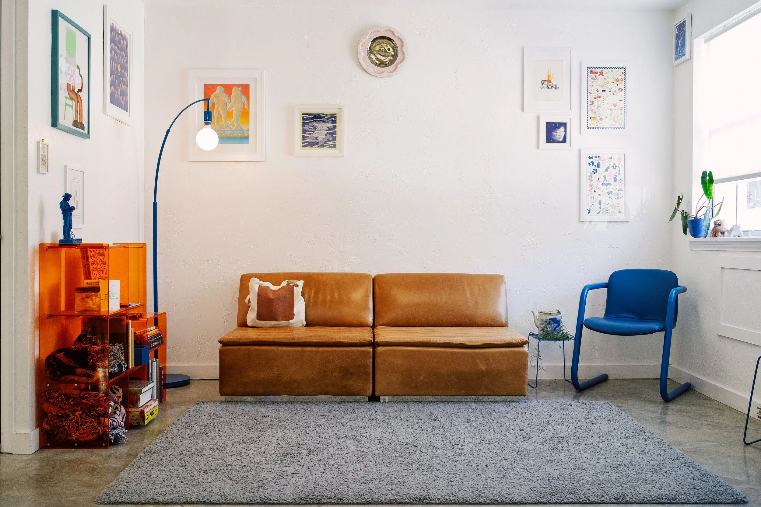 Retro studio waiting area with a tan leather couch, a blue accent chair, and white walls.