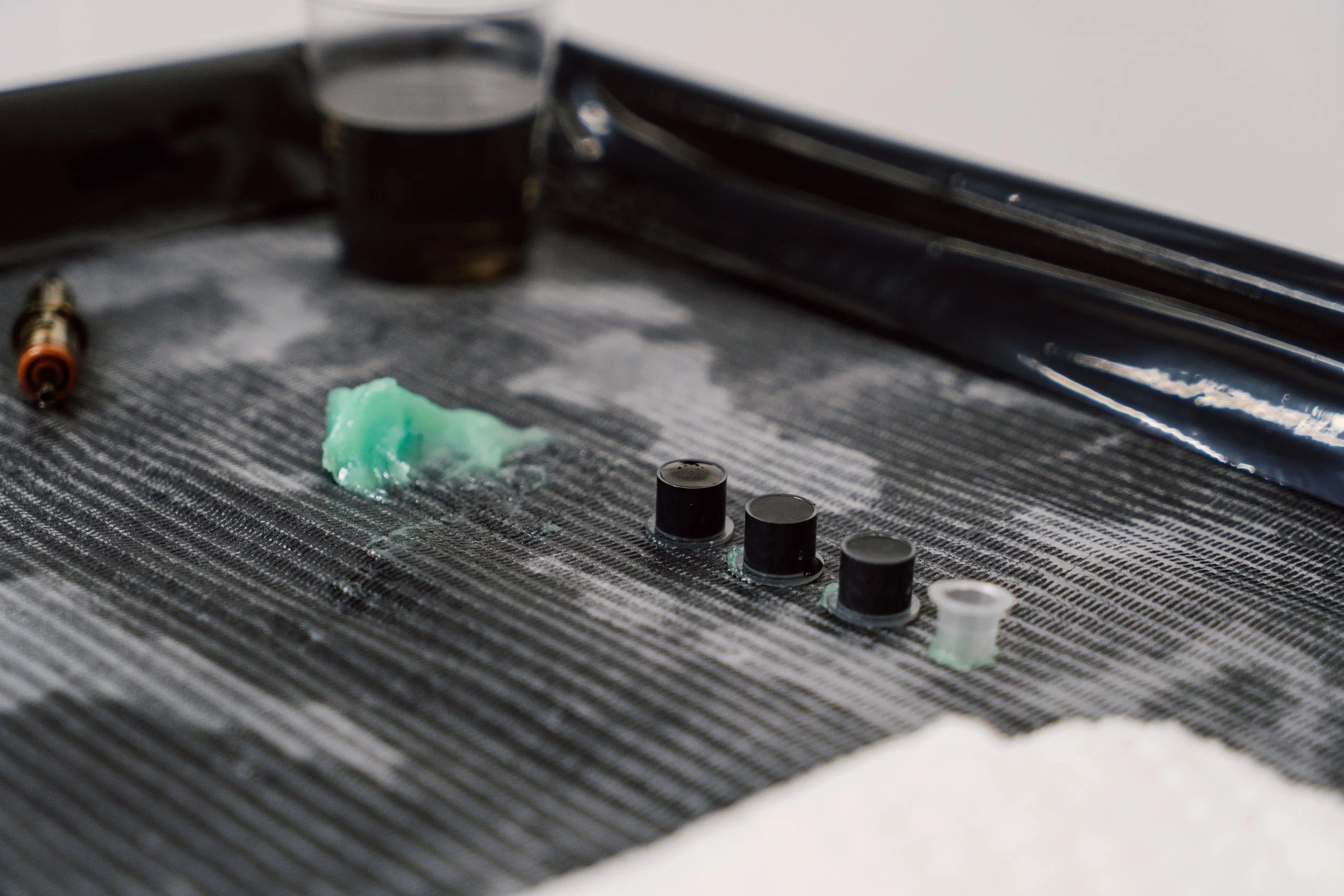 A close-up of a minimalist tattoo setup with ink caps and ointment on a medical tray.