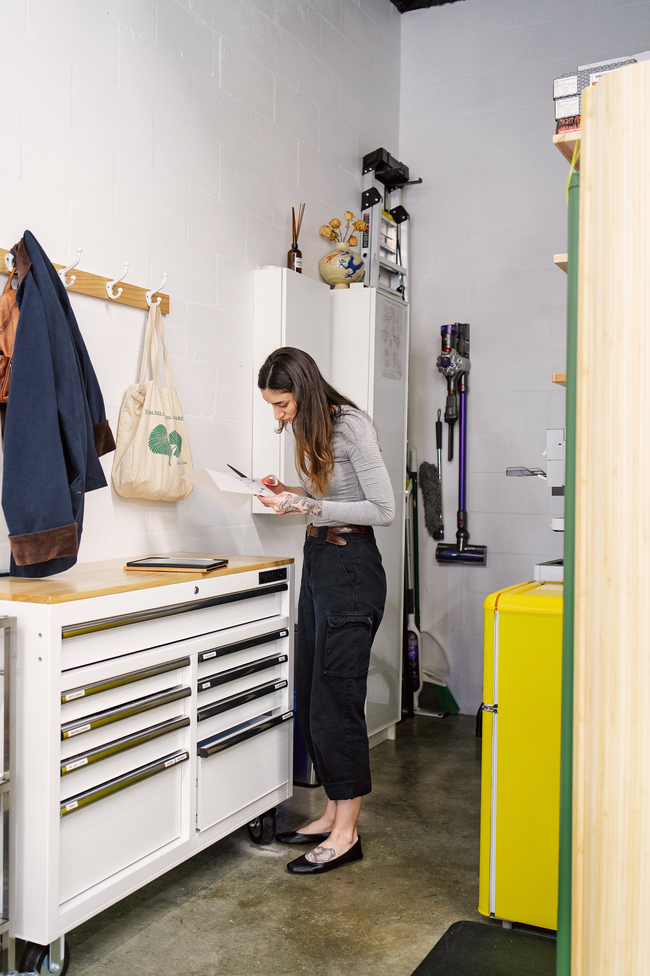 A woman stands at a workbench in the corner of a white room.