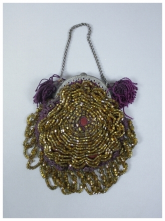 c. 1860 A light brown beaded purse with crocheted purple backing and purple tassels. Silver metal frame and interlinked chain for carrying. There is a row of beaded brown looped fringe along the bottom. The purse is most likely handmade. 