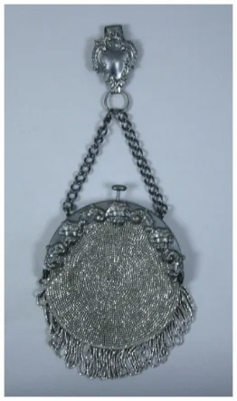 c. 1880 A metal beaded chatelaine purse that is round in shape with tassels on bottom. It has a metal frame with contains 3 cherubs an ornate design. The back of bag is suede and not beaded. Has chain extending from outside of frame on top which connects to an ornate belt clip. There was a note found inside bag with text "Grandma Halughorst bag to be worn on the belt. She made it herself."