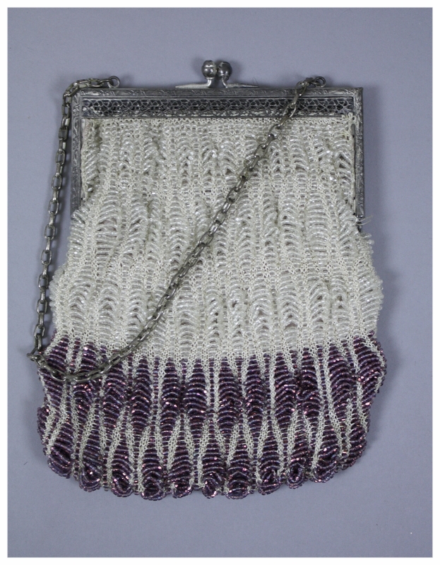  A purple and clear beaded purse. Purse has a crocheted underlayer of white with the purple and clear beads sewn on. The frame is made of silver medal with a floral design and silver metal clasps. Interior of purse is lined with pink sateen. Bag does