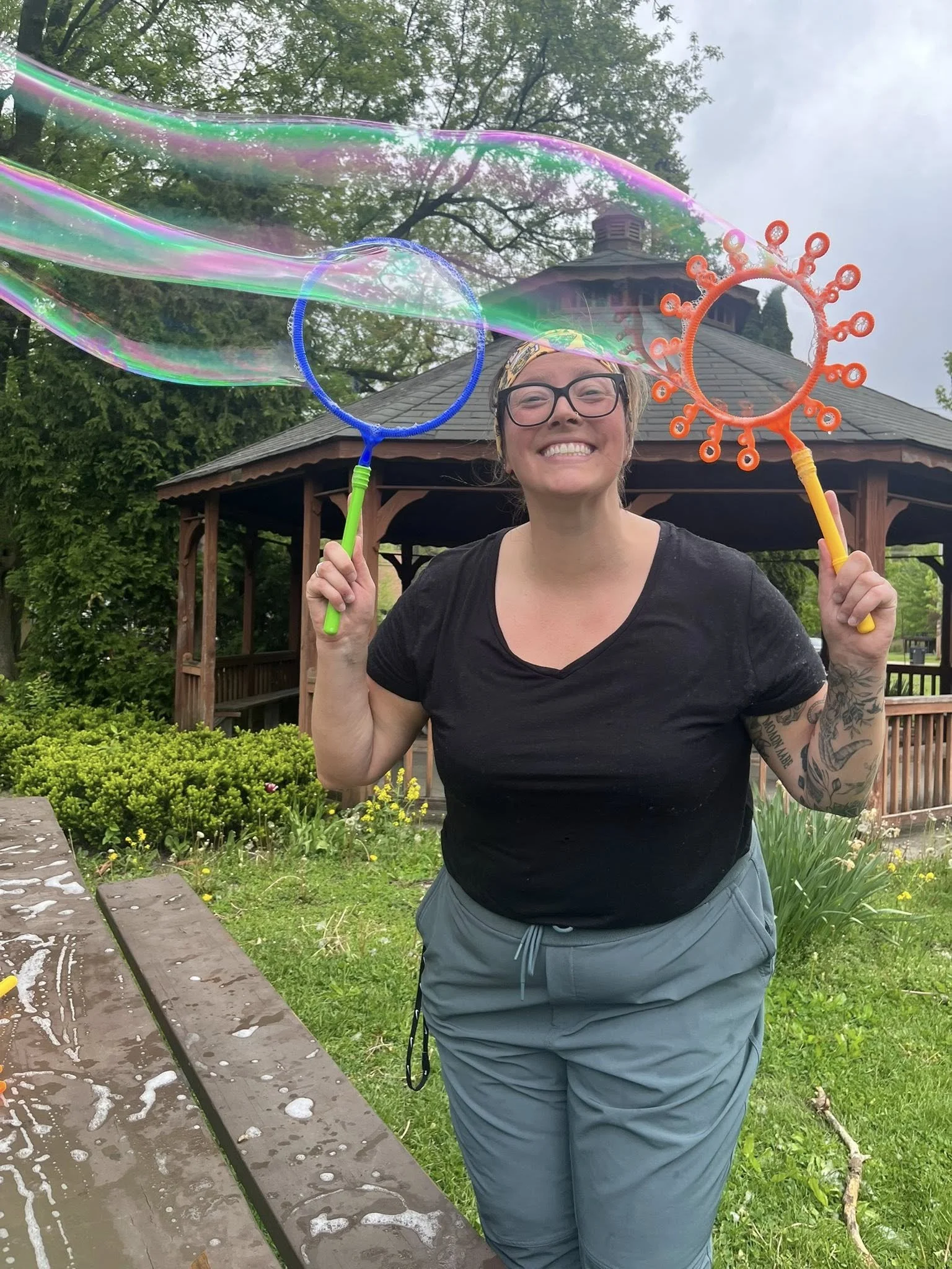 A woman holds two bubble wants and blows a giant bubble.