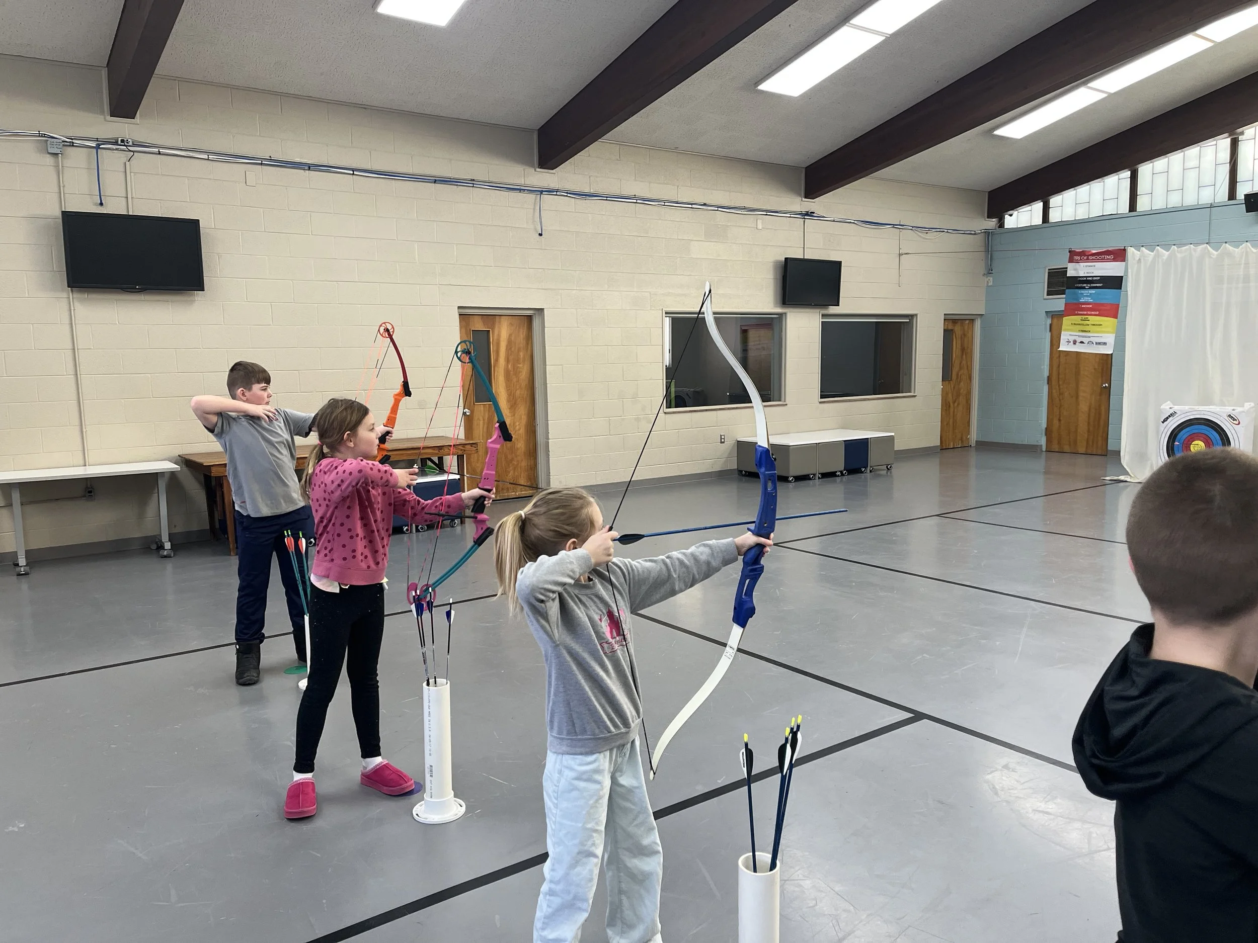 Four kids practice shooting bows and arrows.