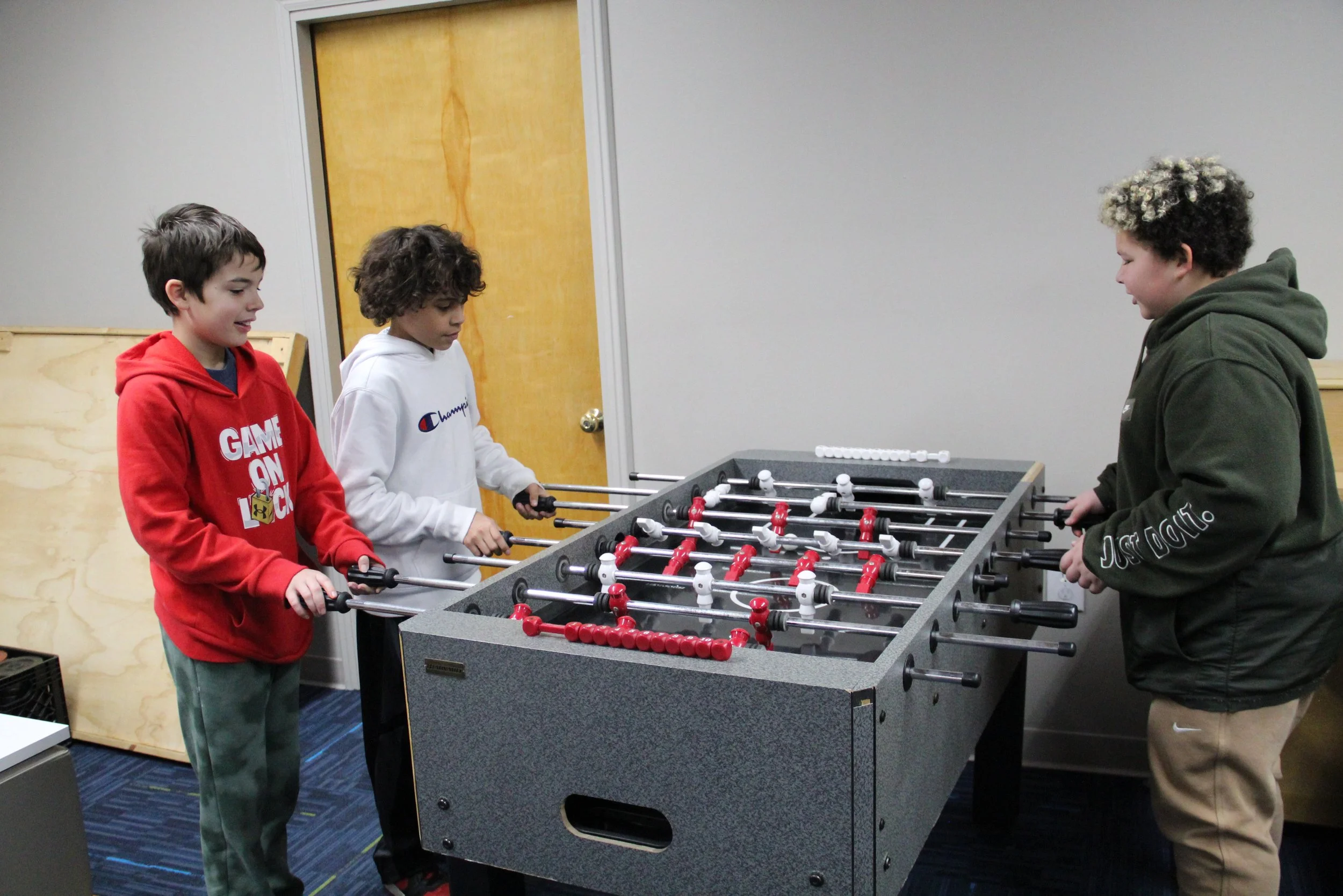 A picture of a group of kids playing fooseball at the Hive Teen Center.
