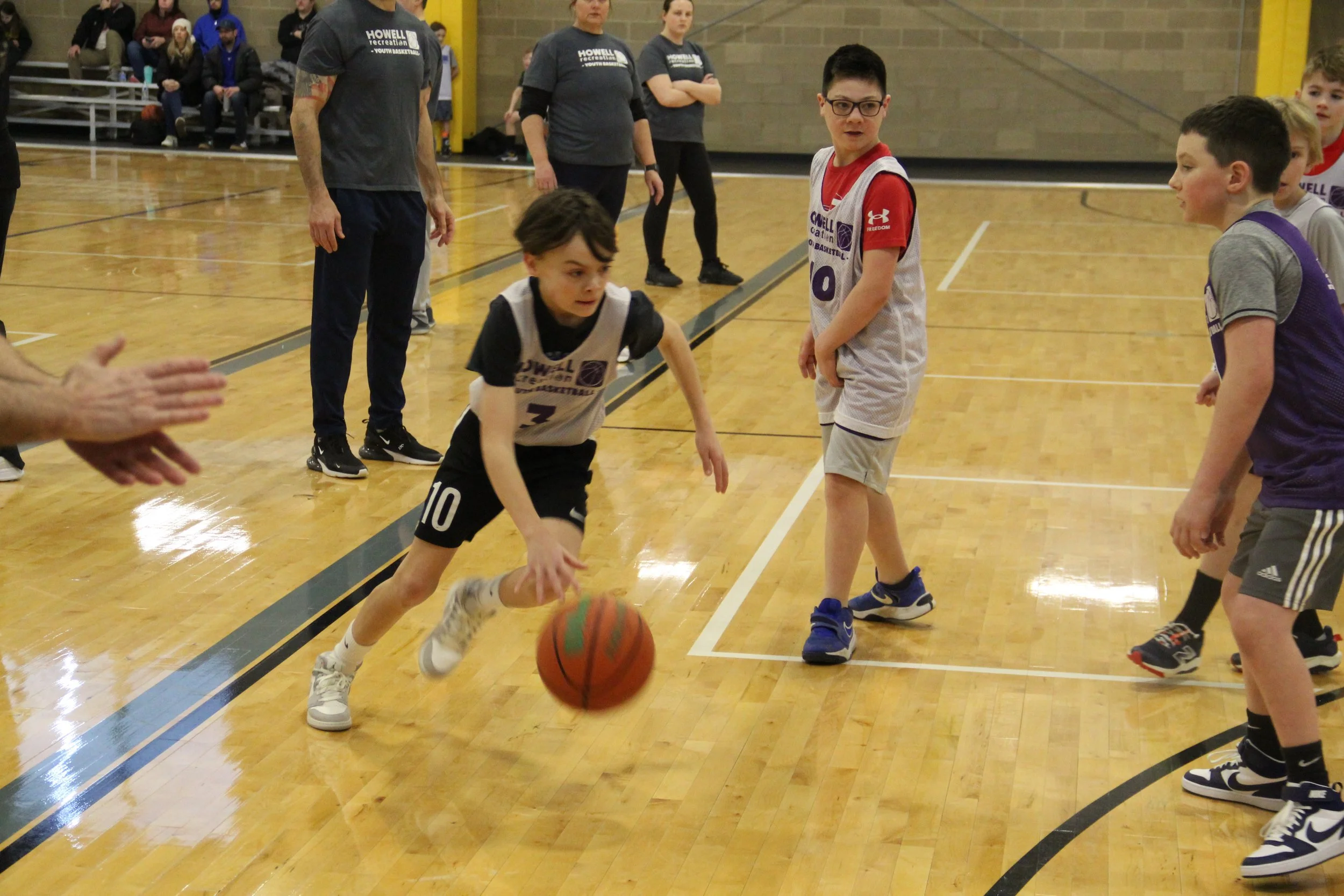 A boys furiously dribbles a basketball through a crowd of other players.