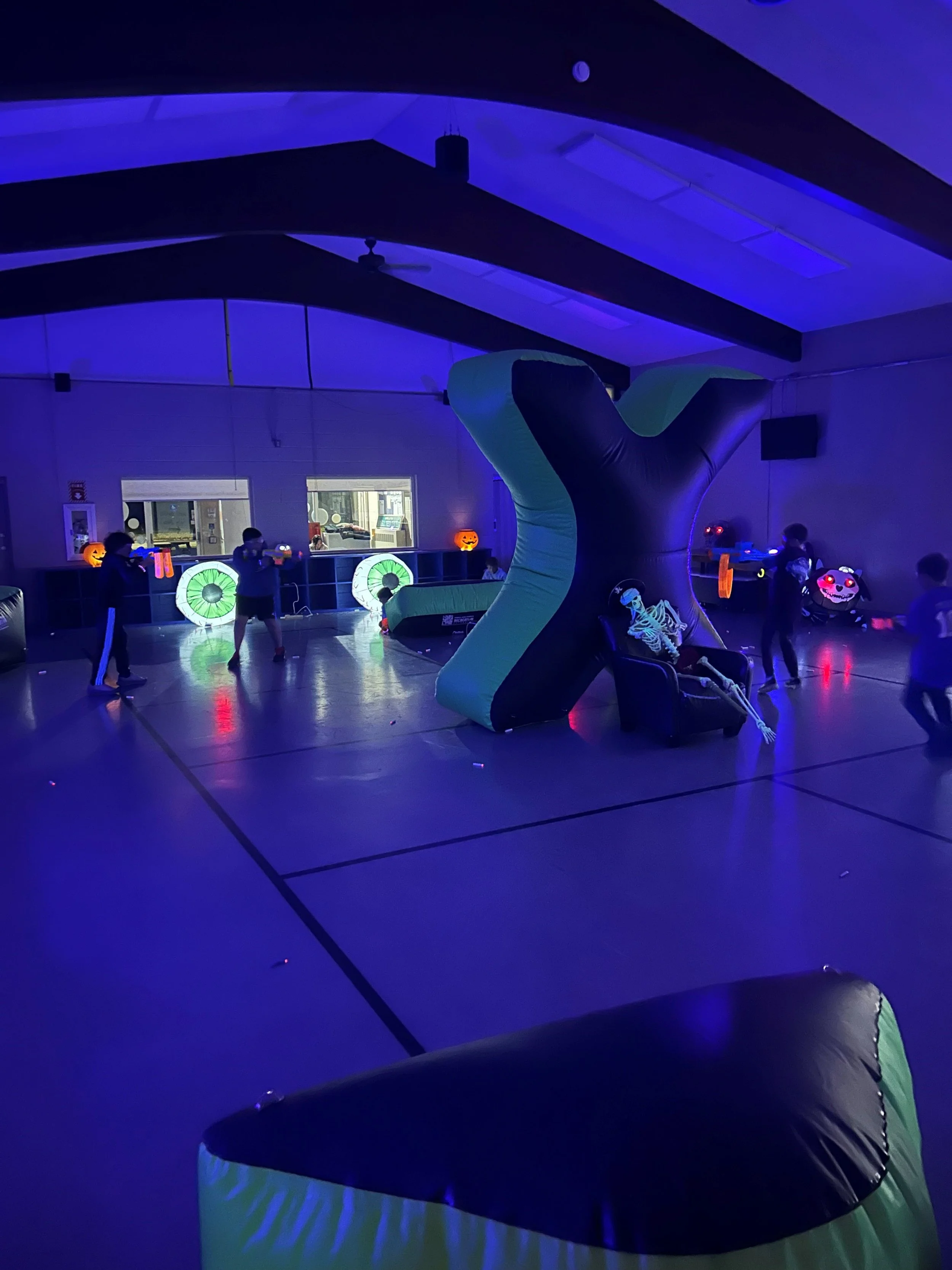 A group of kids plays with NERF blasters in a space illuminated by glow lights.