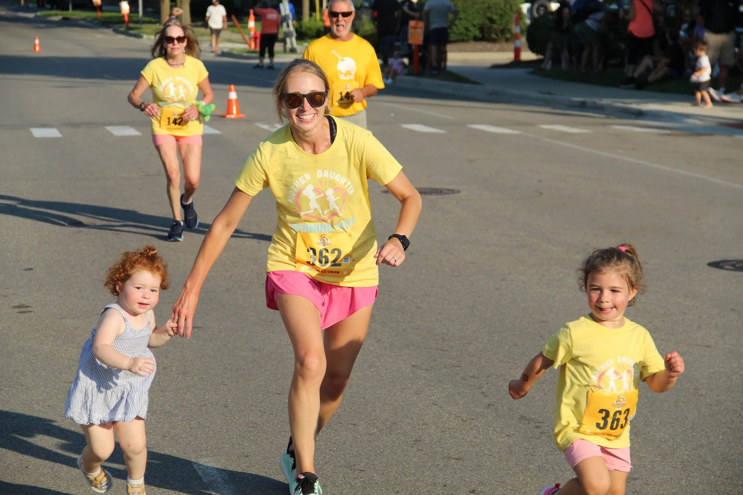A mom and two little girls run towards the finish line at the Melon Run 1 Mile event.