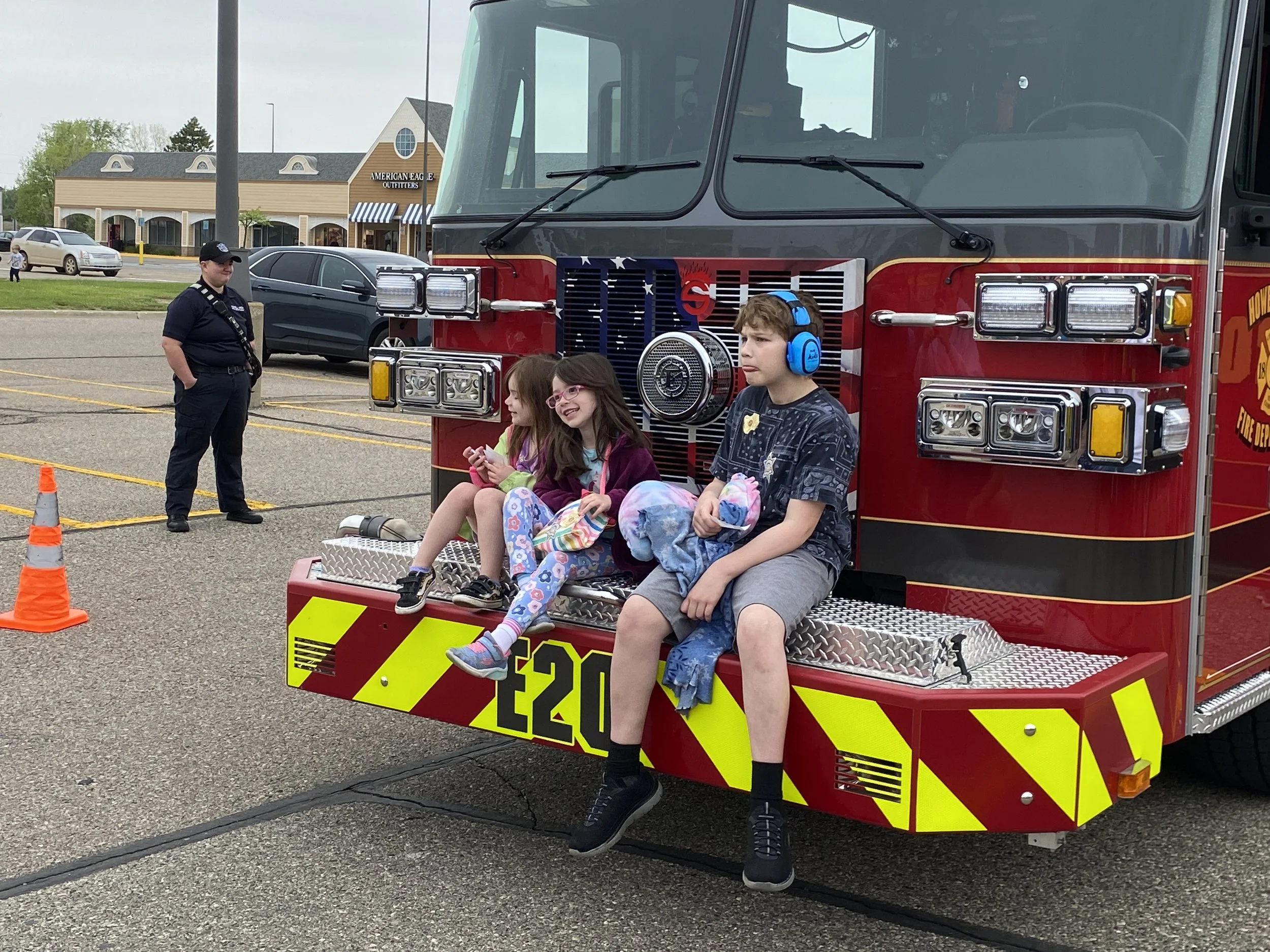 A group of kids smile as they sit on the front bumper of a fire truck.